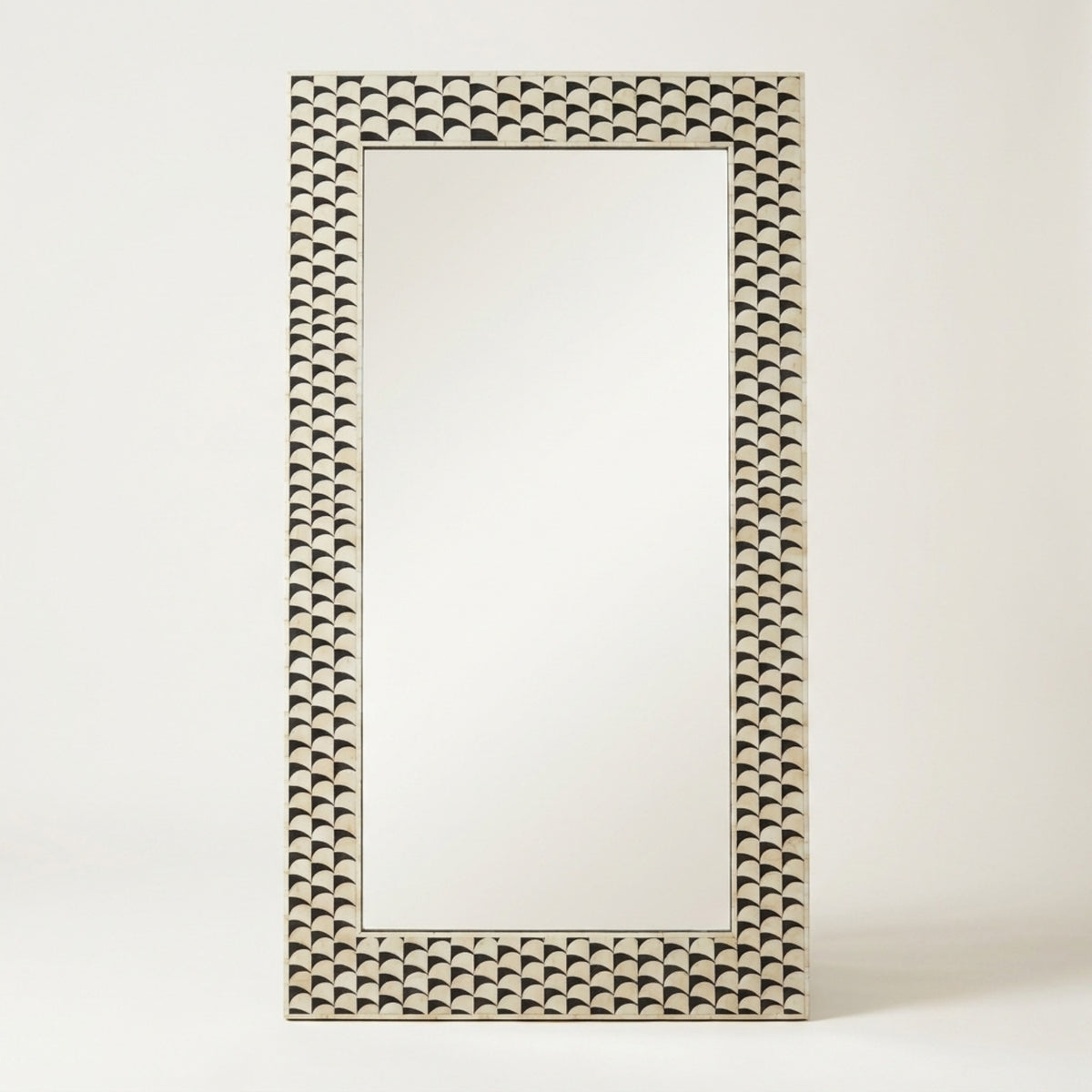A rectangular wall mirror with an ornate, textured frame featuring a repeating scalloped shell-like pattern in a warm beige and dark brown tone, set against a plain off-white background.
