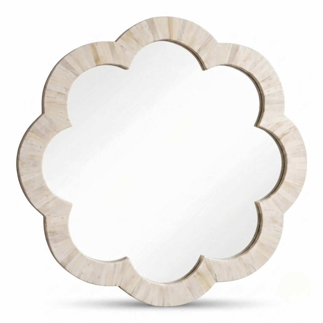 A scalloped cloud-shaped wall mirror with a light natural stone frame hangs above a minimalist console table in a bright, modern room with a large window.