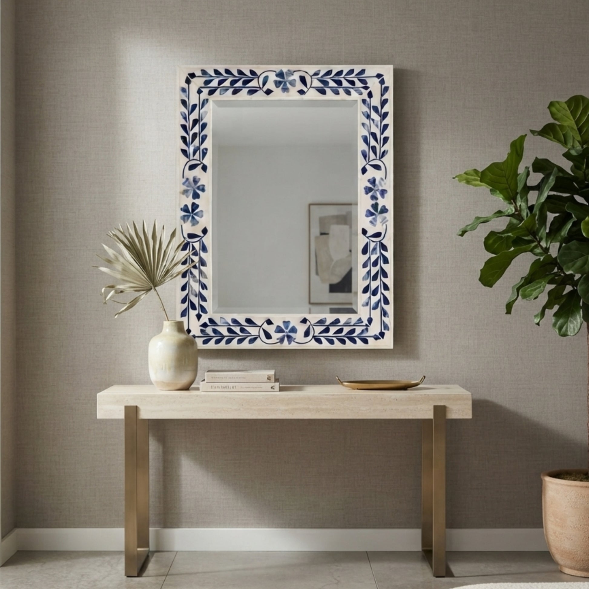 A rectangular wall mirror with a white frame decorated with blue floral and leaf motifs, hanging on a textured gray wall above a light wood console table with decorative items.