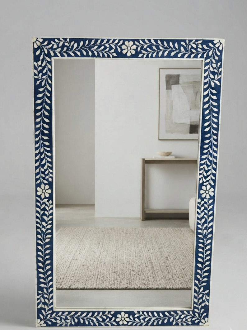 A rectangular wall mirror with a decorative frame featuring a navy blue and white floral vine pattern, shown on a light gray background with a softly blurred interior reflection.