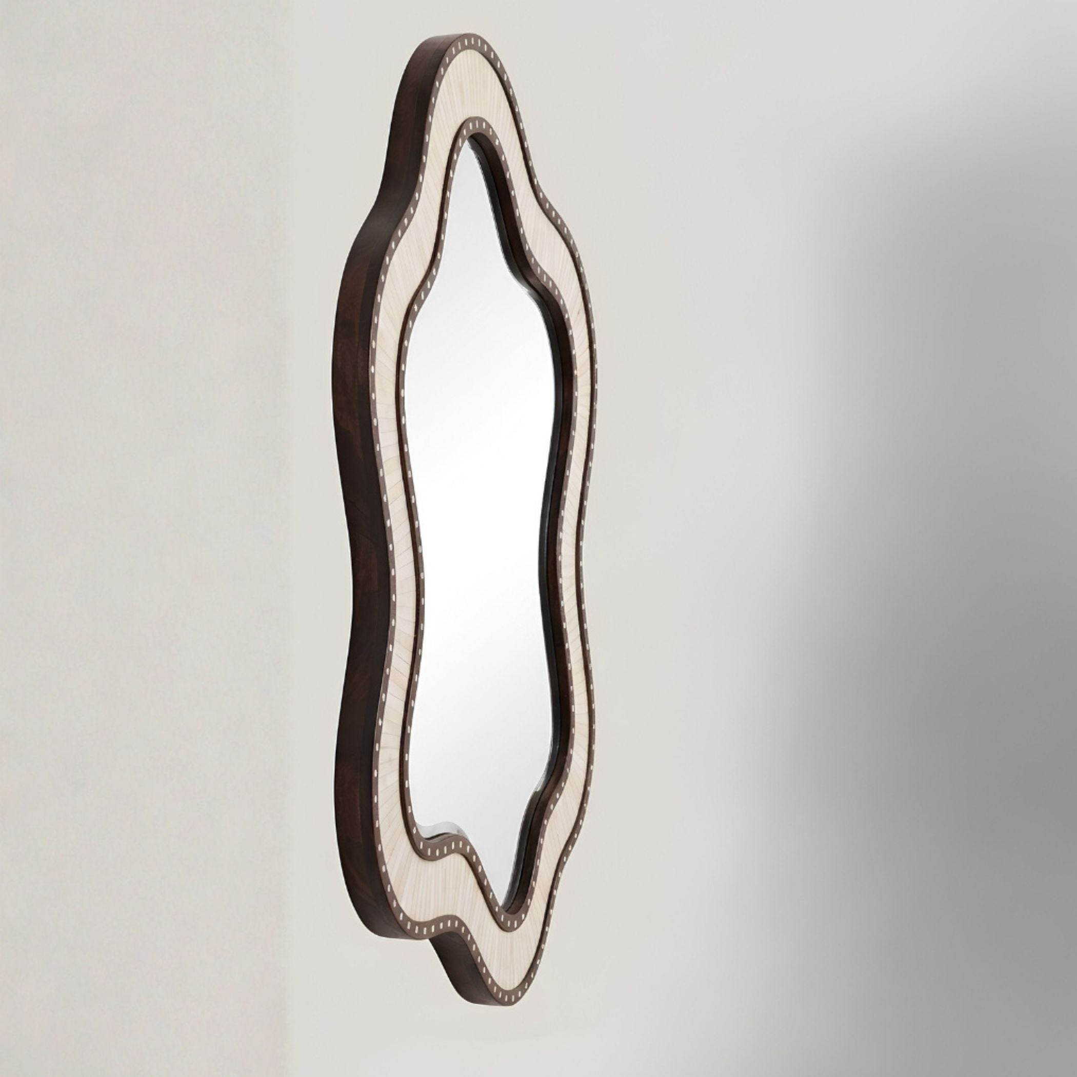 An asymmetrical scalloped wall mirror with a dark brown frame and a light beige inner border, shown against a neutral light gray wall.