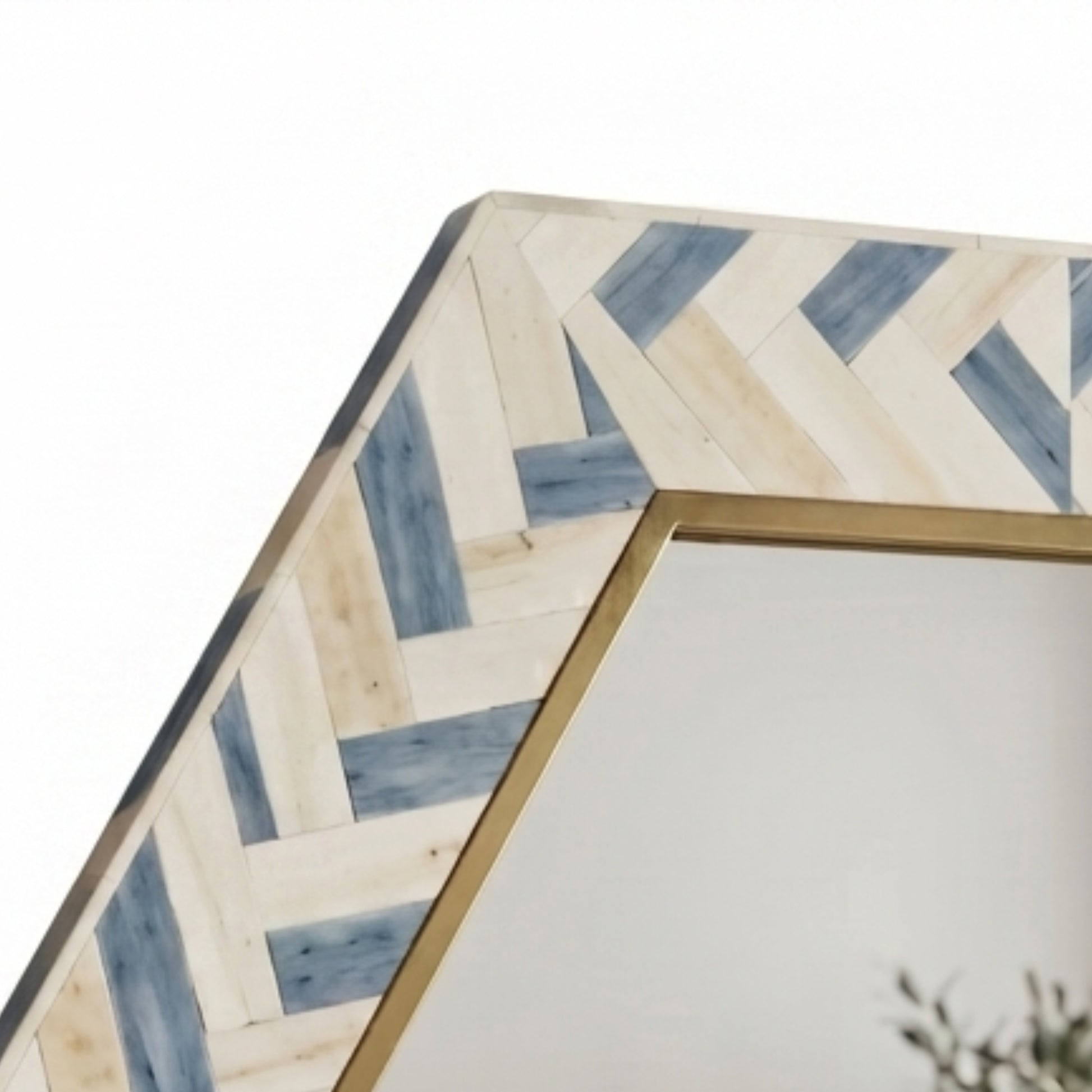 Close-up of a hexagonal mirror with a geometric inlay border made of light beige and blue wood pieces, framed in gold-toned metal.