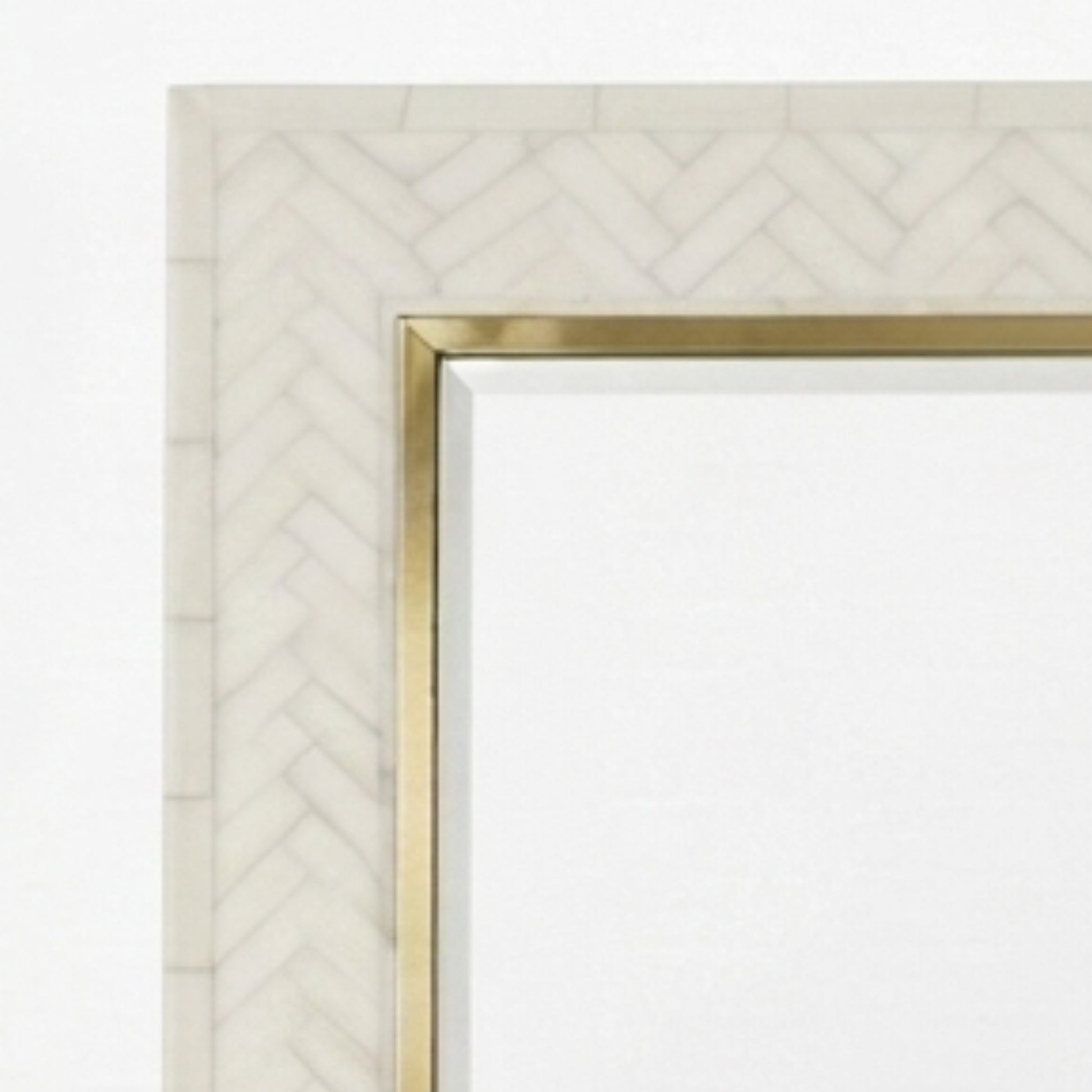 Close-up of a rectangular mirror frame with a white herringbone patterned border and a slim gold metal trim.