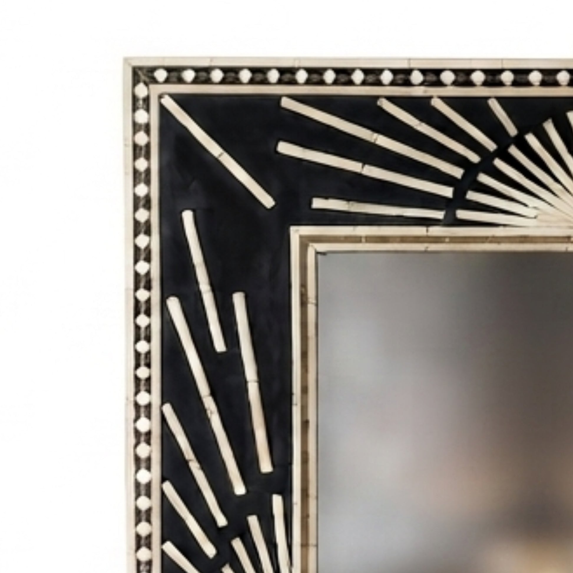 Close-up of a decorative rectangular mirror frame with a black and beige sunburst inlay design, showing part of the reflective mirror surface.