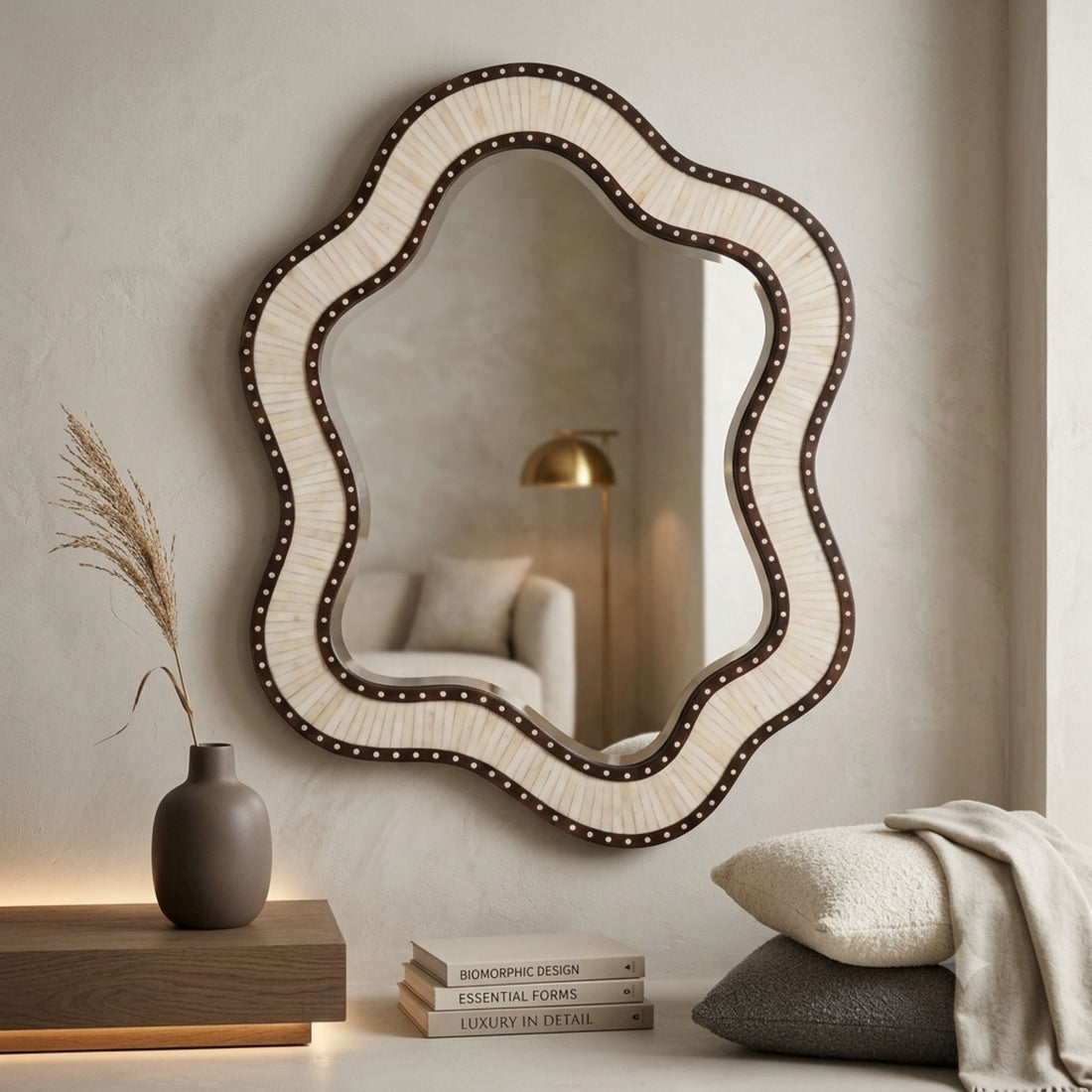 An asymmetrical scalloped wall mirror with a cream and dark brown woven frame and metallic studs, styled in a warm, modern interior setting.