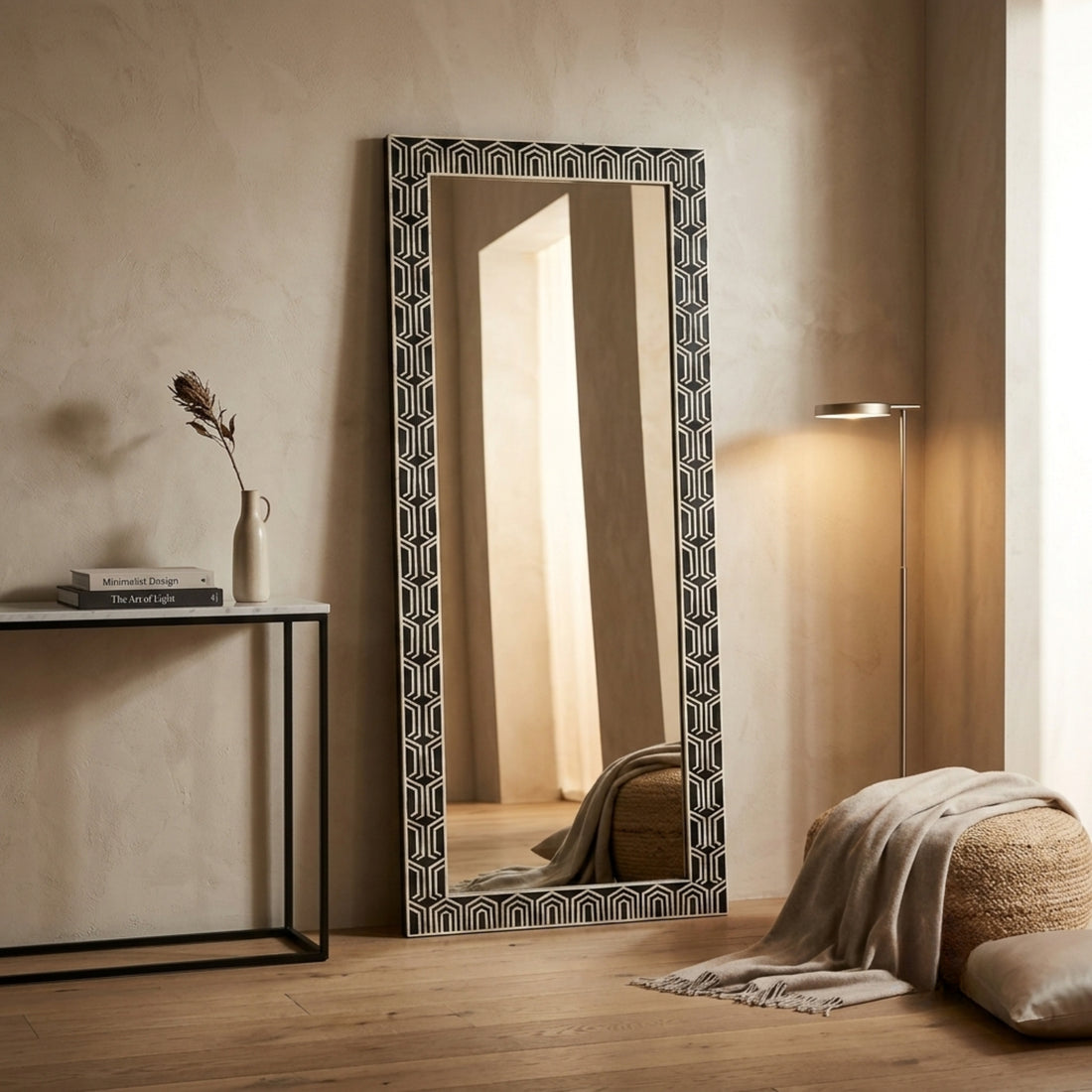 A tall rectangular floor mirror with a black and white geometric patterned frame, styled in a warm, modern room next to a console table and a floor lamp.