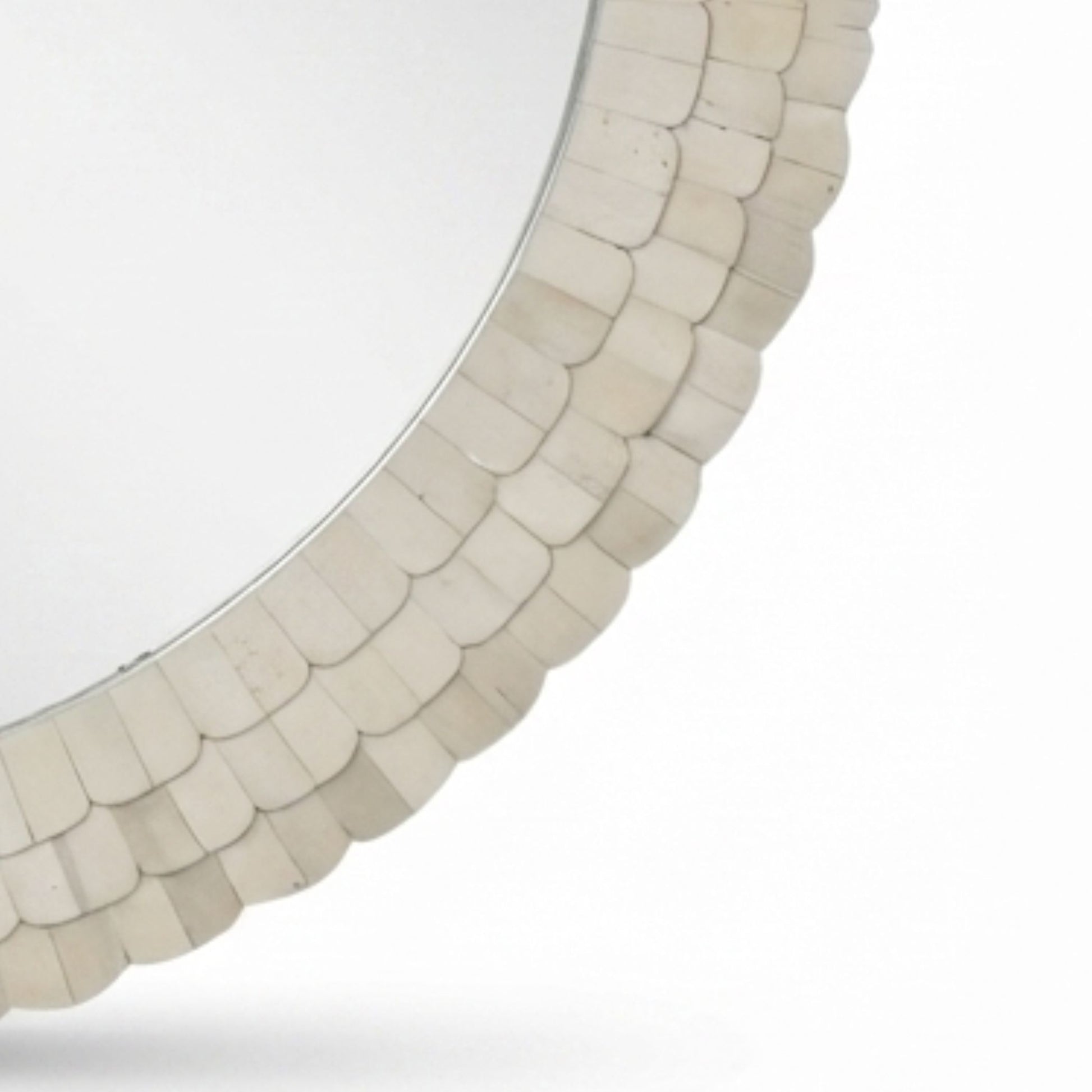 A close-up of a round wall mirror with a decorative border made of overlapping scalloped shell-like pieces in a warm off-white or cream tone, shown against a plain white background.