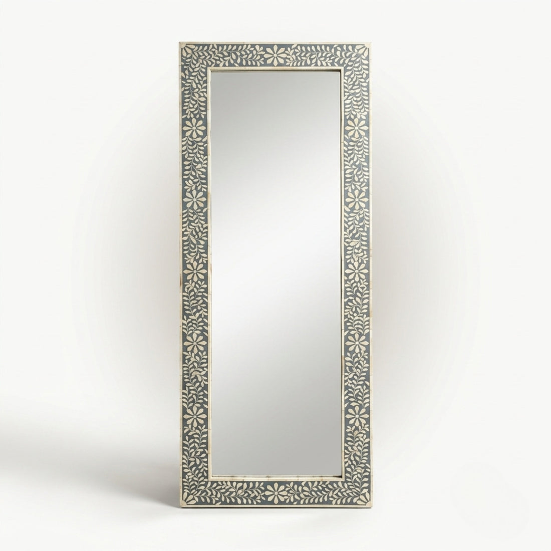 A tall rectangular wall mirror with an ornate carved frame featuring a repeating floral or starburst pattern in light beige on a gray background, shown against a plain light gray studio backdrop.