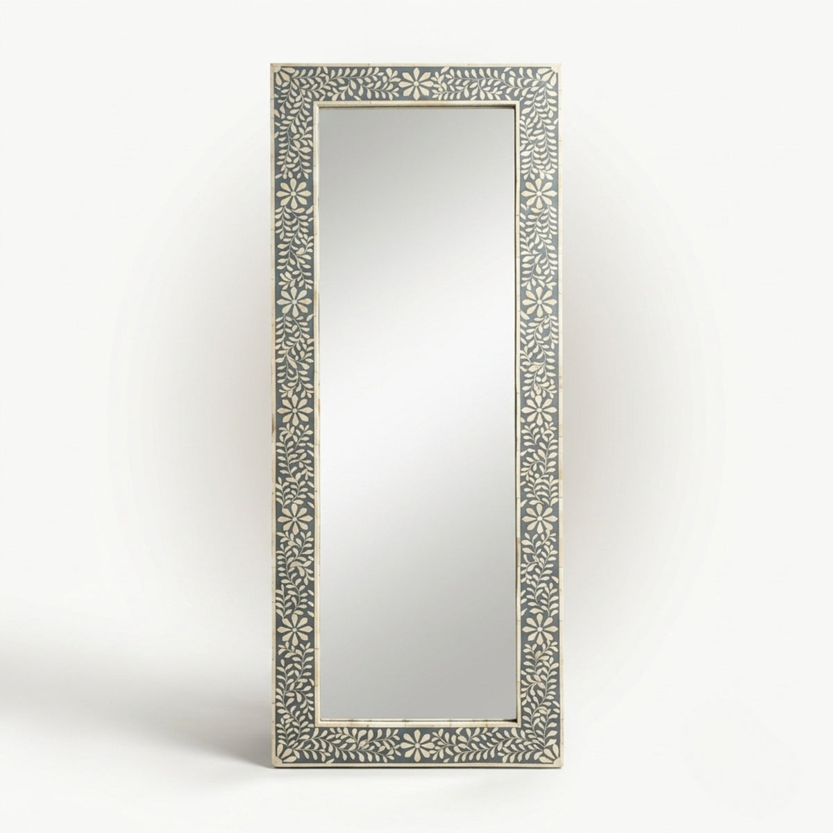 A tall rectangular wall mirror with an ornate carved frame featuring a repeating floral or starburst pattern in light beige on a gray background, shown against a plain light gray studio backdrop.