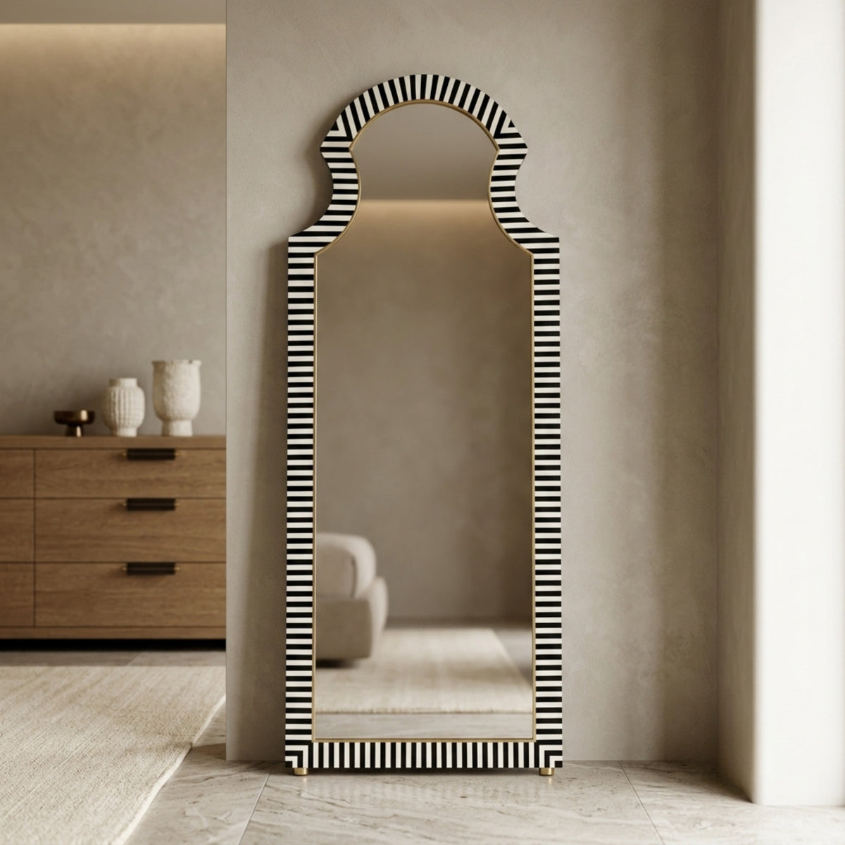 A tall full-length floor mirror with a black and white striped frame, leaning against a textured beige wall in a modern interior setting.