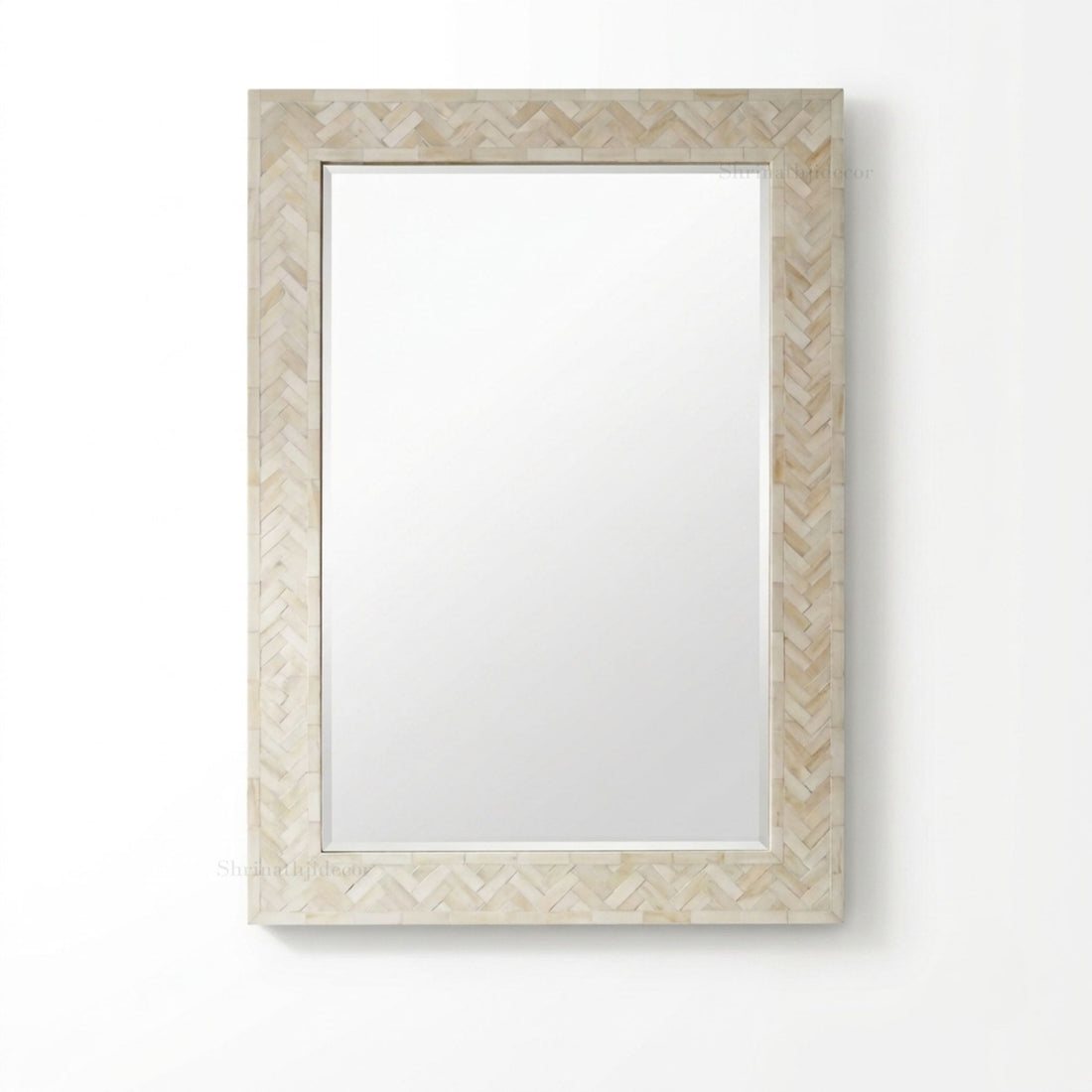 A rectangular wall mirror with a light beige herringbone-patterned frame, mounted on a textured beige wall above a dark wood console table. The mirror reflects a window and dried plants, and a small brass lamp sits on the table.