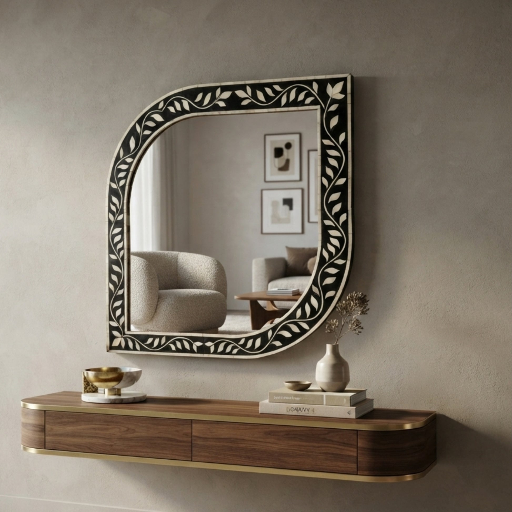 An arched wall mirror with an ornate black and white bone-inlay frame, mounted on a textured gray wall above a floating wooden console shelf with brass trim.