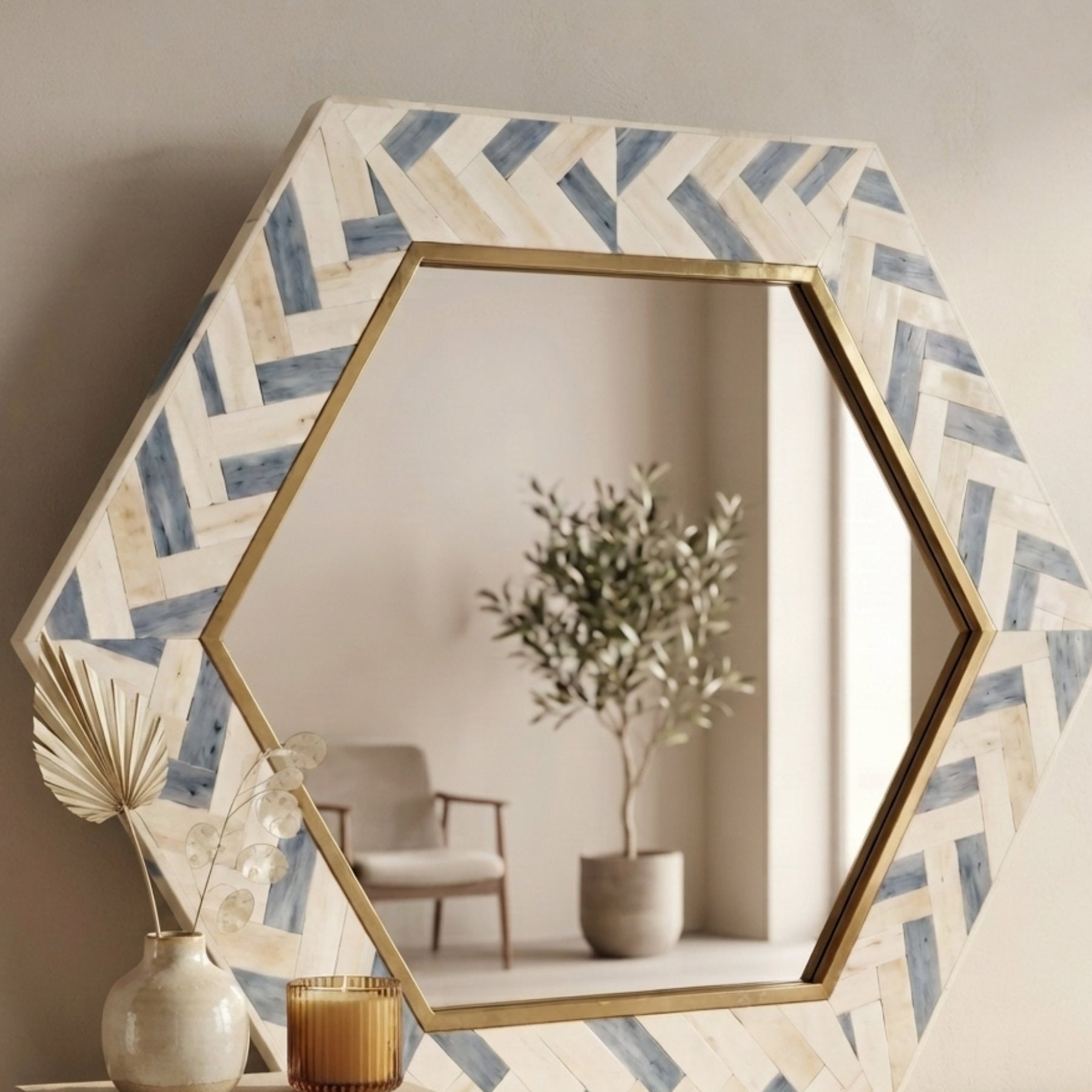 Hexagonal wall mirror with a blue and cream herringbone patterned frame and a gold inner border, styled on a wooden console table with decorative vases and books.