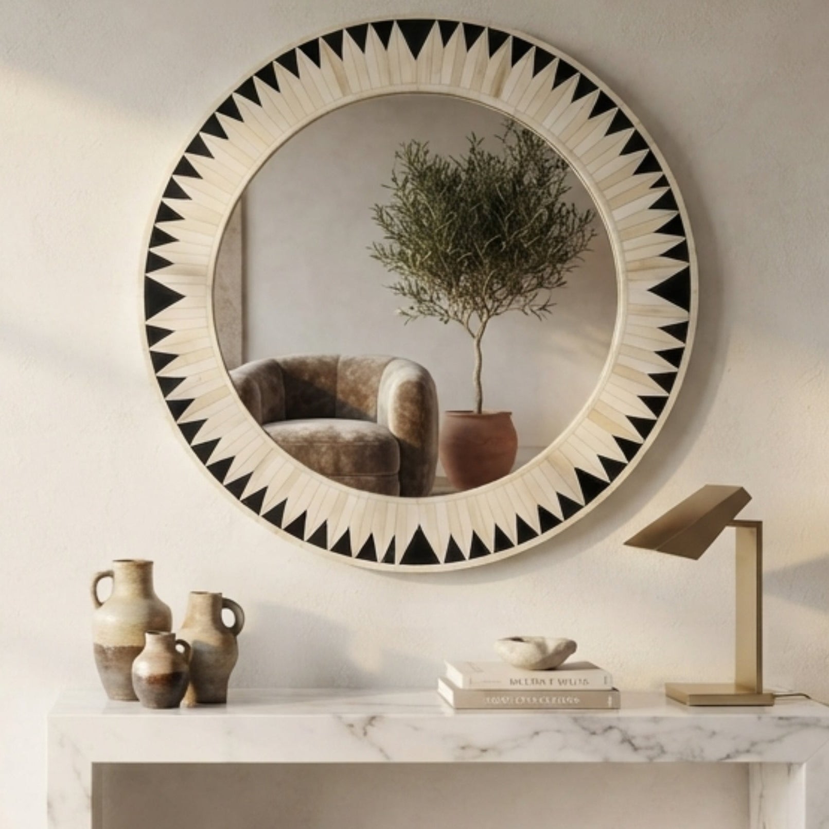 A large round wall mirror with a black and white geometric sunburst frame hangs above a white marble console table in a styled interior room.