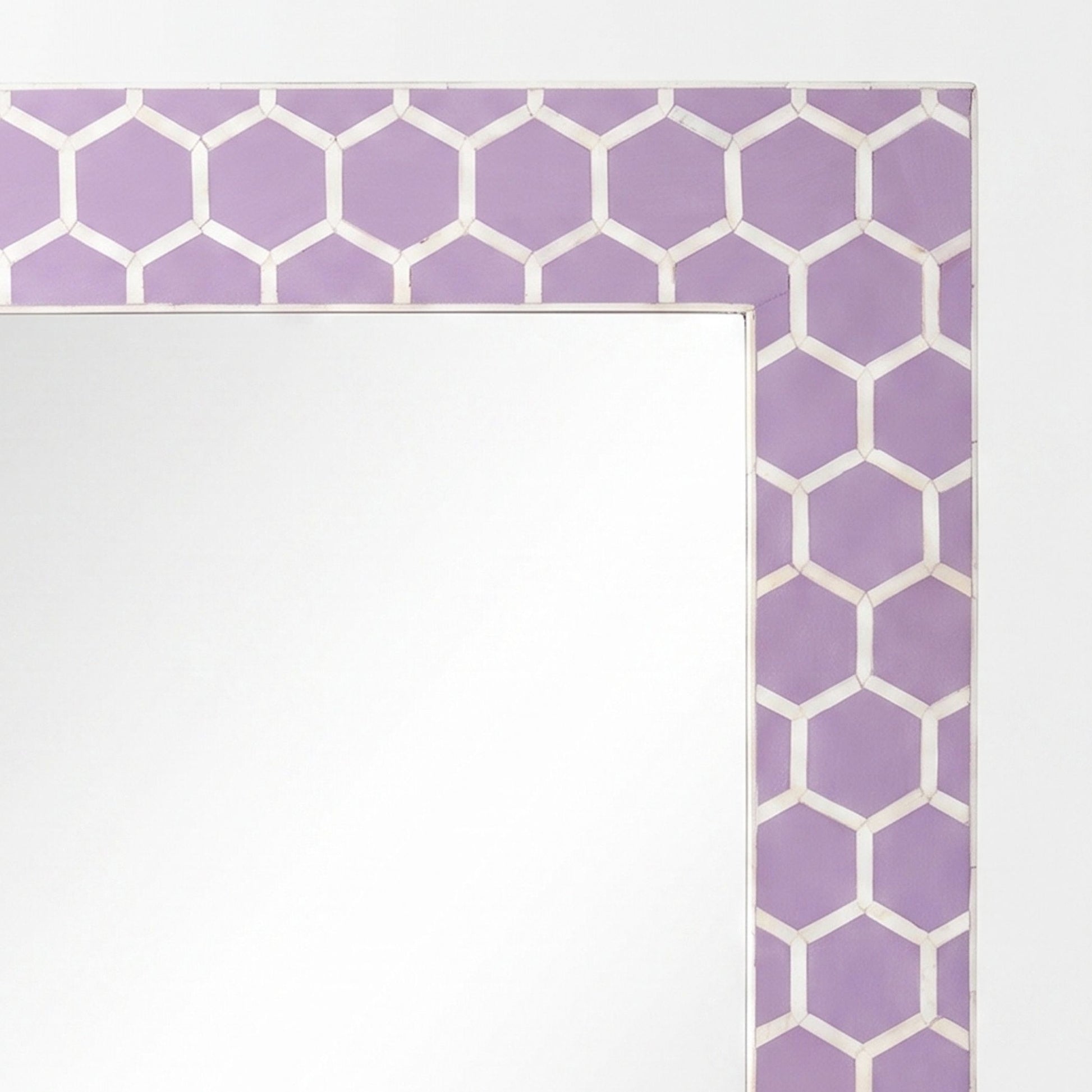 A close-up of a decorative mirror frame with a lavender purple and white geometric hexagon pattern, showing a blank reflective mirror surface.