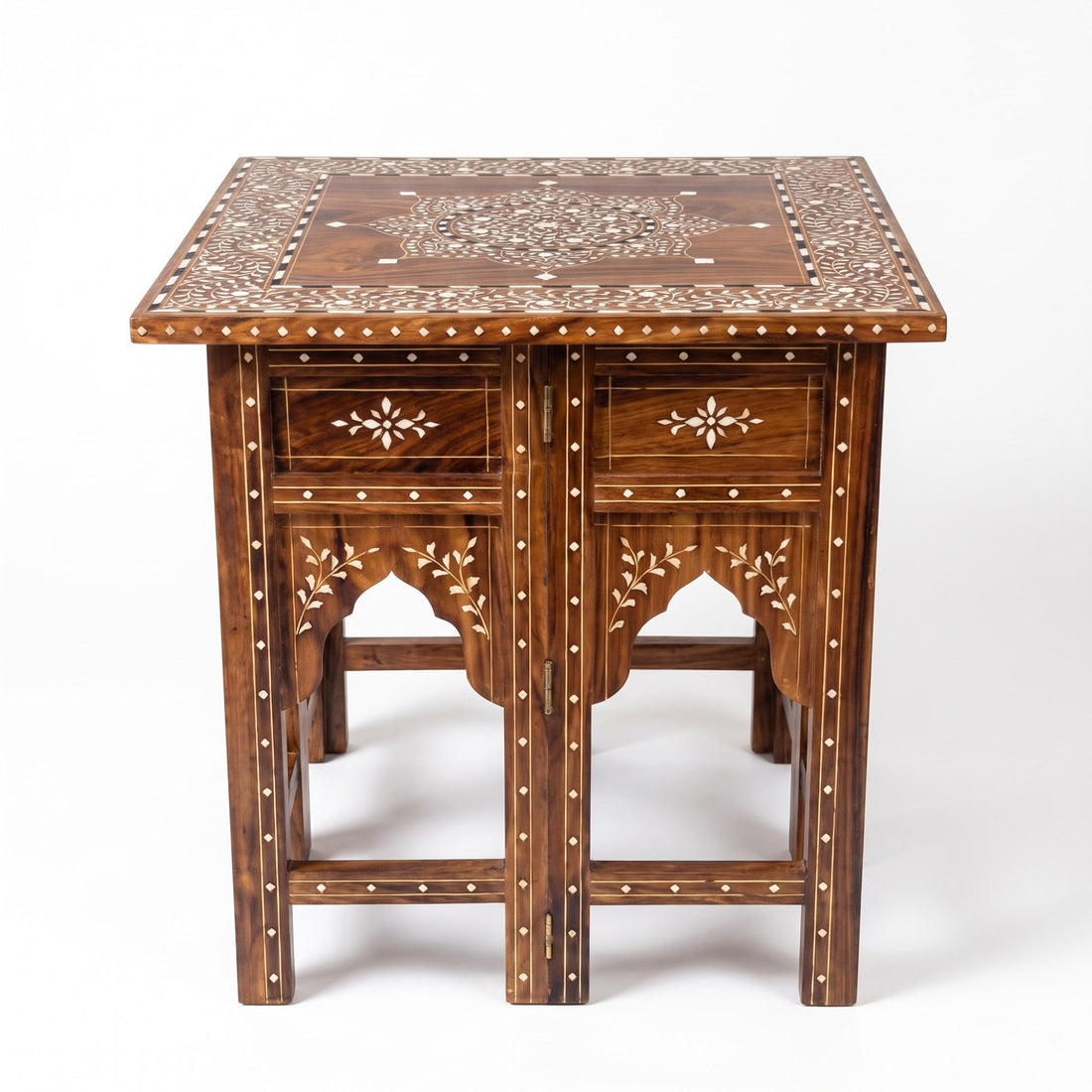 An ornate dark brown wooden end table with intricate mother-of-pearl inlay on the top and carved legs, styled in a bright room on a jute rug next to a potted plant.