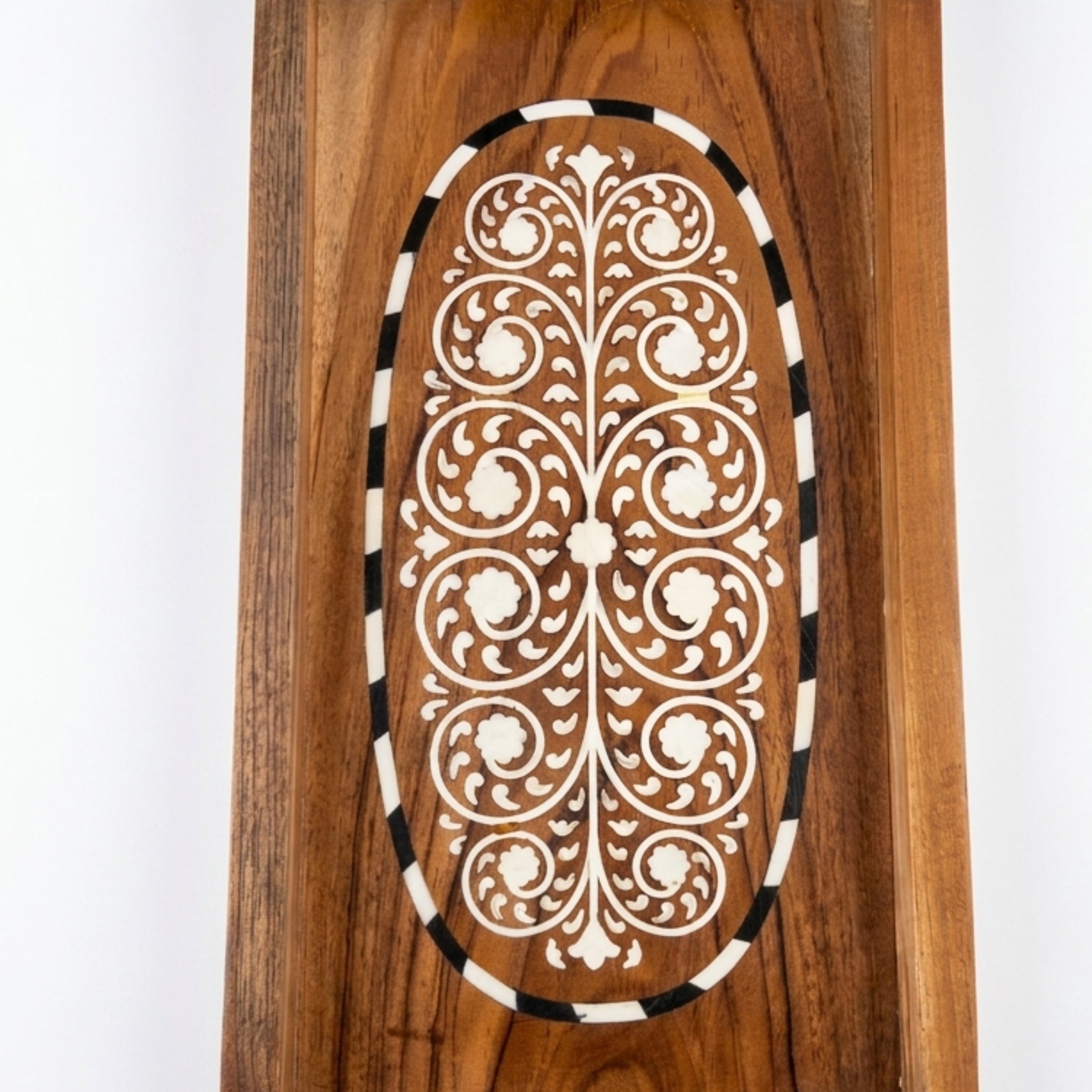 A close-up of a wooden decorative panel featuring an oval inlay with intricate white floral and scrollwork patterns, bordered by alternating black and white stripes, set against a plain white background.