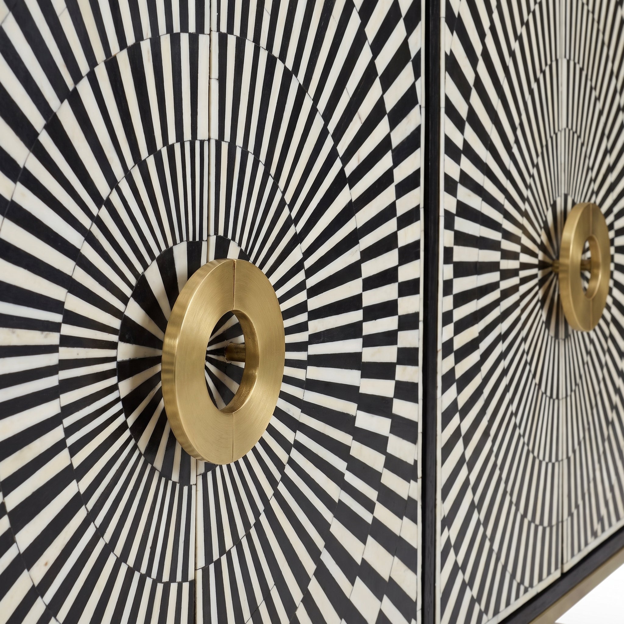 Close-up of a decorative cabinet or door featuring a black and white radial striped sunburst pattern with large circular gold handles.