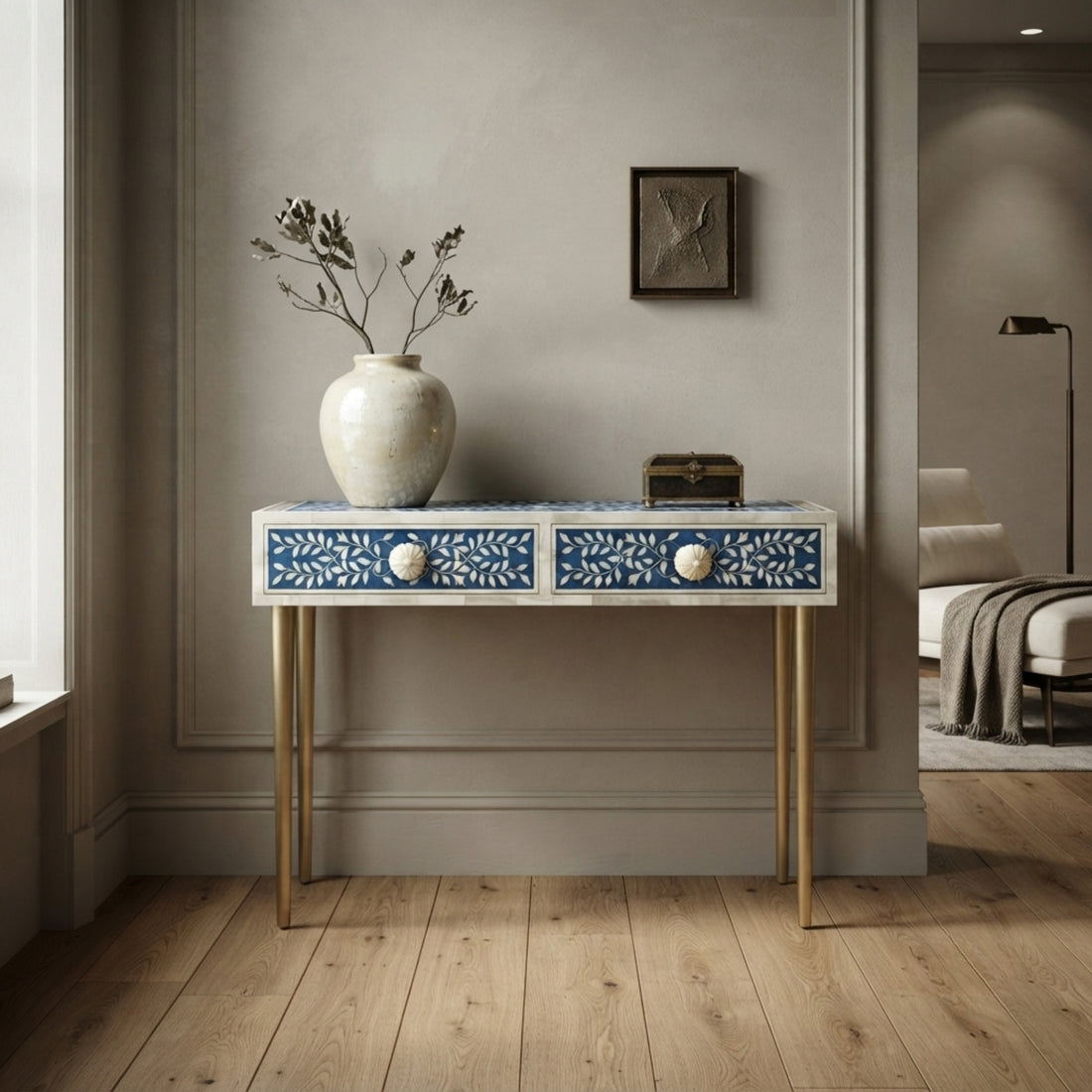 A decorative console table with two blue and white patterned drawers and gold legs, styled in a modern entryway with a vase and small box on top.