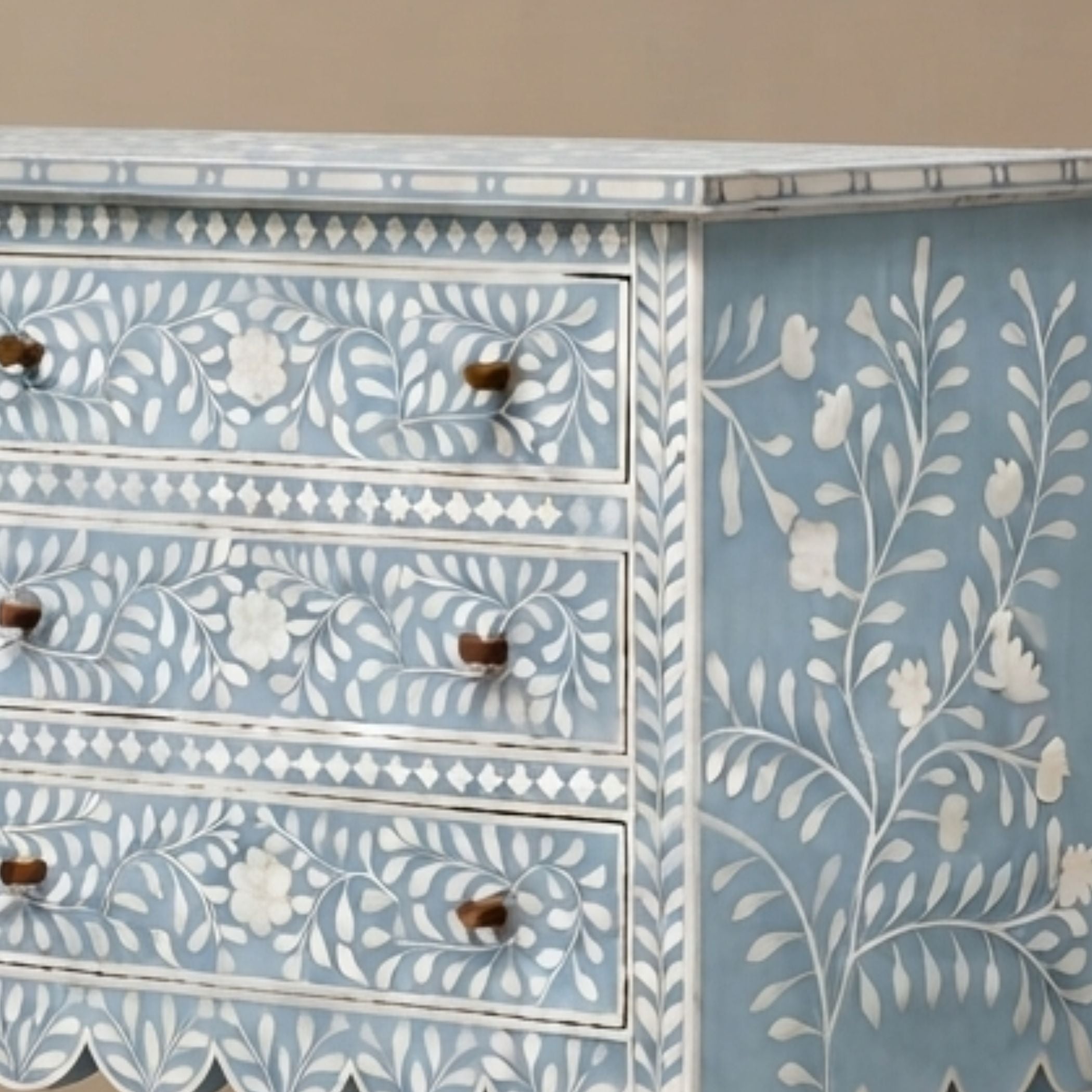 A light blue and white decorated wooden chest of drawers with floral inlay patterns and small brown knobs.