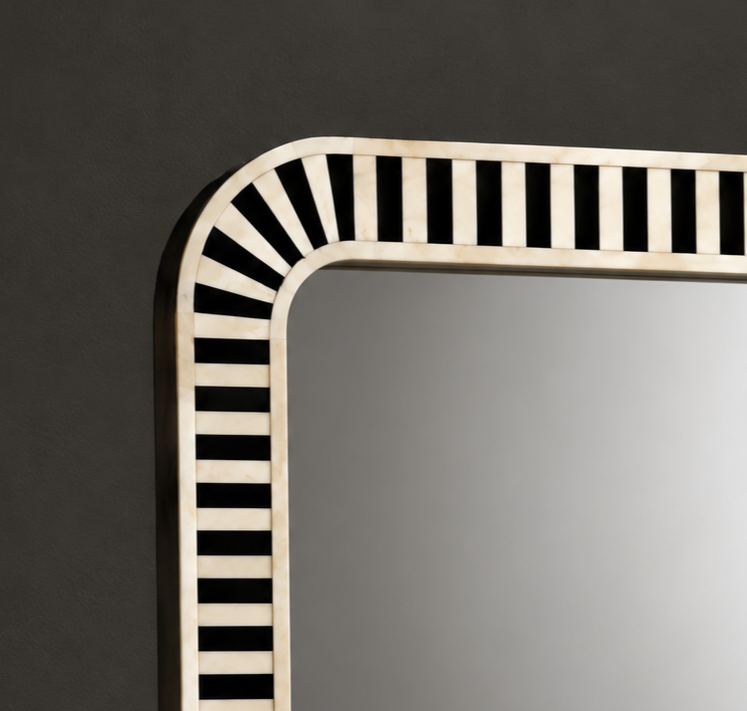 Close-up of a decorative rectangular mirror with a curved top-left corner and a black-and-ivory striped frame, shown against a dark gray wall.