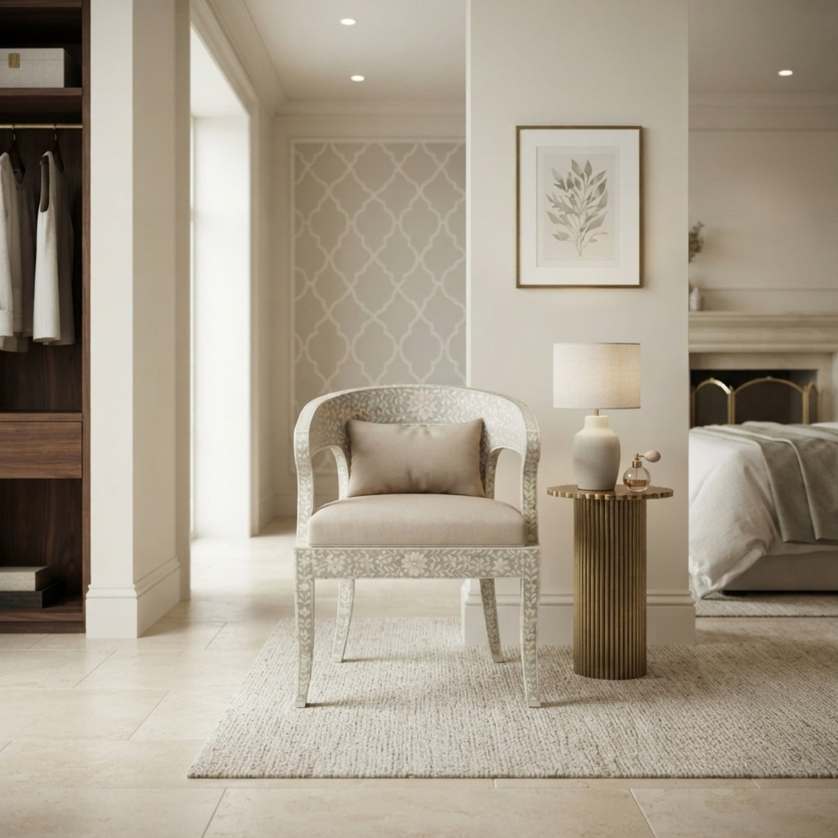 A light beige upholstered armchair with a white patterned frame and a matching pillow, styled in a bright, modern bedroom setting next to a gold side table with a lamp.