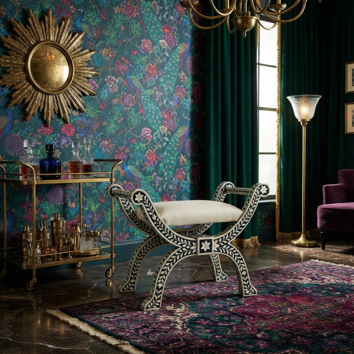 An ornate black and white carved bench with a cream cushion sits in a richly decorated room with floral wallpaper, a gold sunburst mirror, a brass bar cart, dark green curtains, and a purple rug.