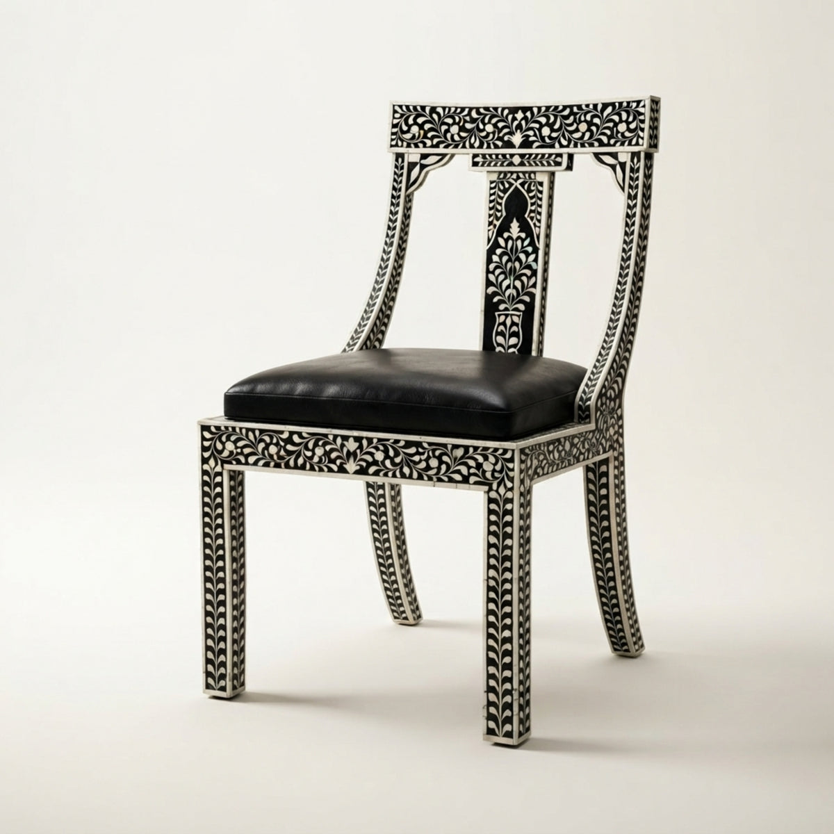 An ornate black and white carved wooden dining chair with a black leather seat cushion, shown against a plain light background.