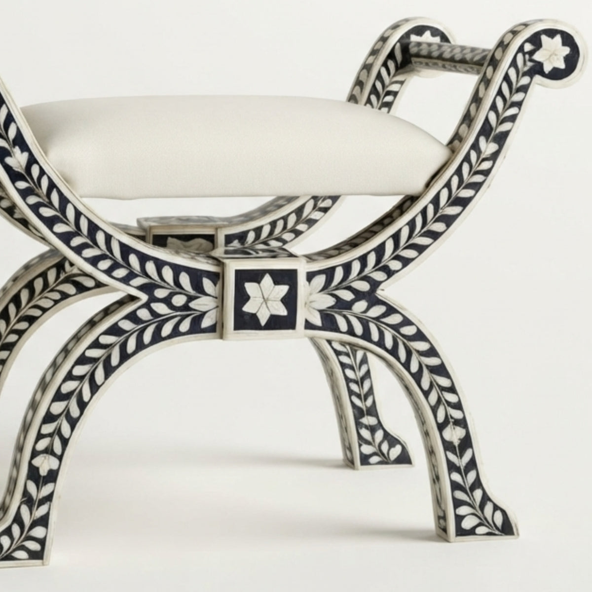 A close-up of an ornate bench with a white upholstered seat and carved dark blue and white inlay detailing on the frame, shown against a plain white background.