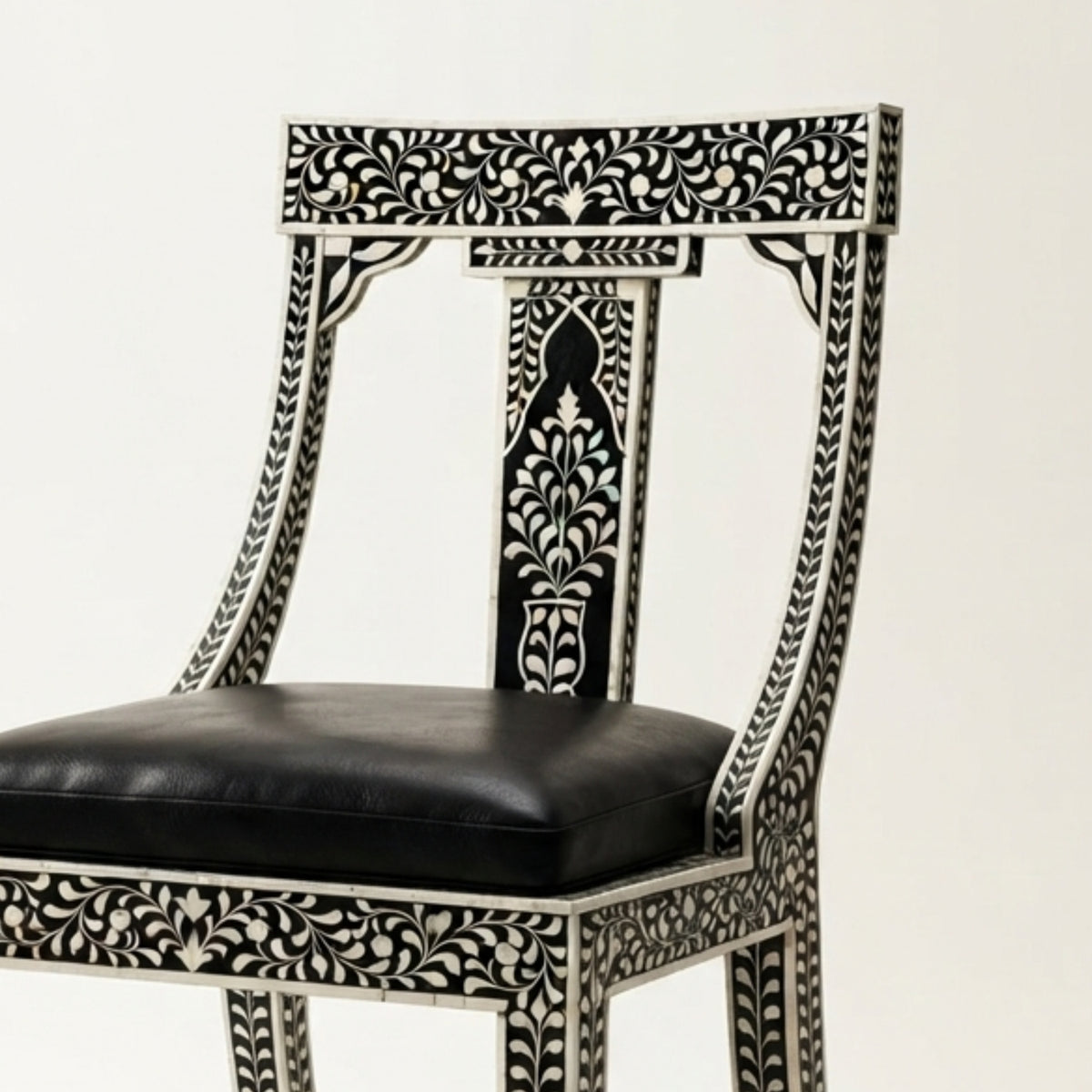 An ornate black and white carved wooden chair with a black leather seat cushion, shown against a plain off-white background.