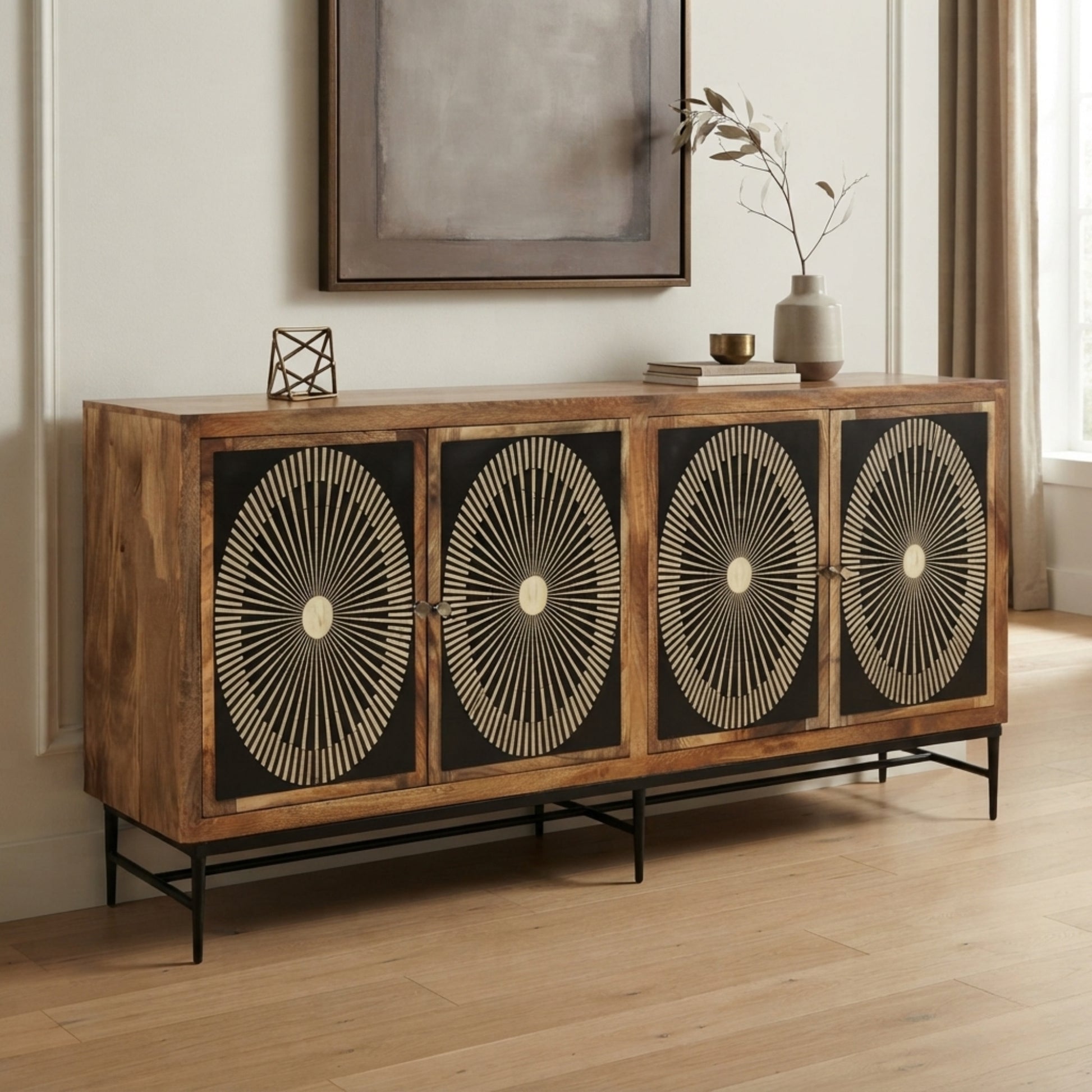 A rustic wooden sideboard console with four doors featuring black panels and cream sunburst geometric patterns, styled in a bright living room setting.