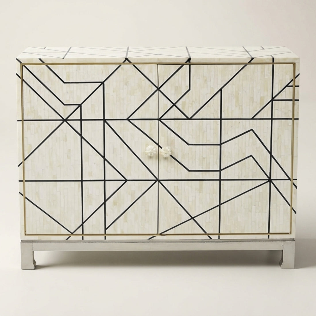 A modern sideboard cabinet with a geometric black wireframe pattern over a light beige wood-grain finish, styled in a bright, contemporary living room.