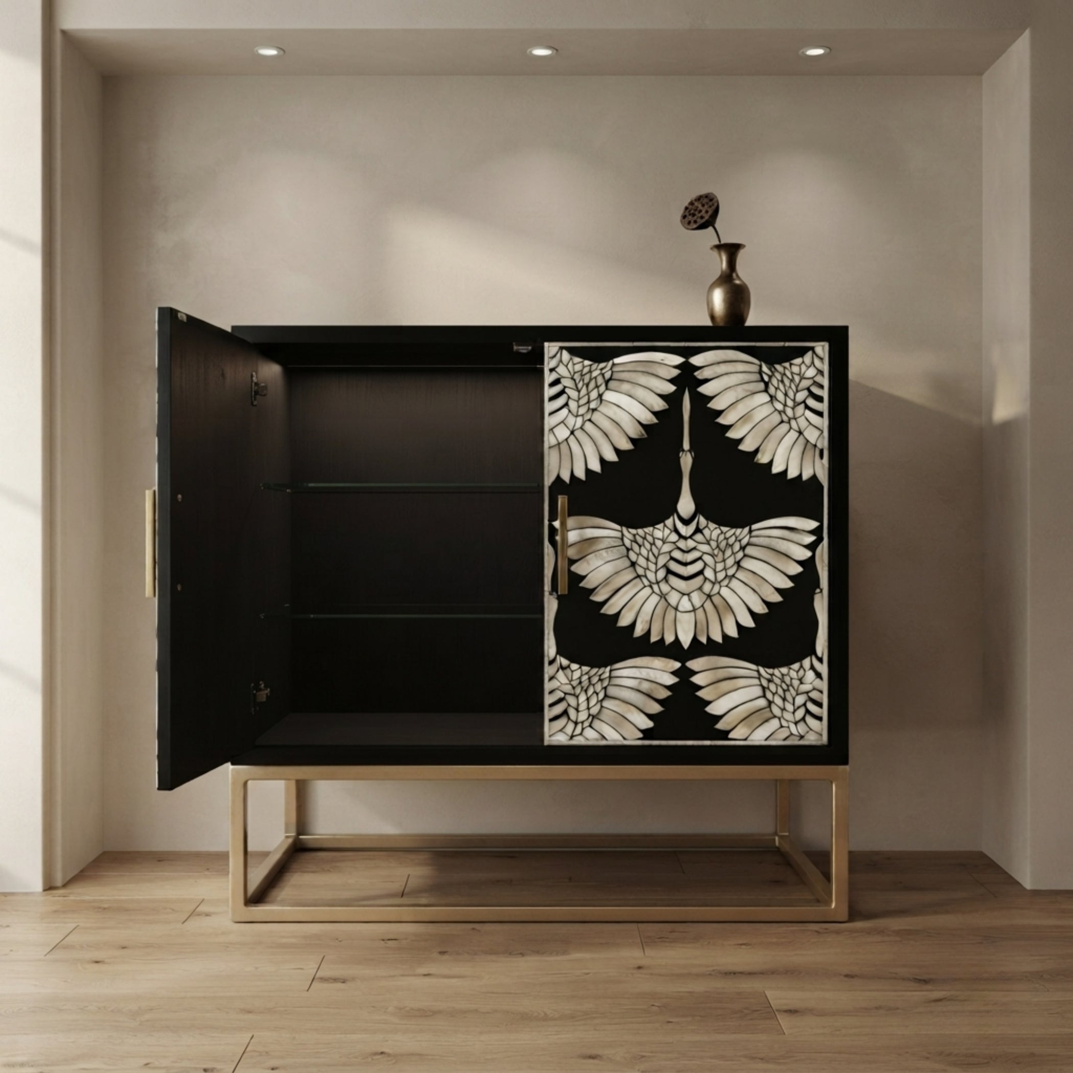 A black wooden sideboard cabinet with a gold metal frame and legs, featuring a decorative door panel with a white and black bird motif. The cabinet is shown open with its left door swung to the left, revealing three interior shelves, set against a neutral beige wall with recessed ceiling lights and a light wood floor.