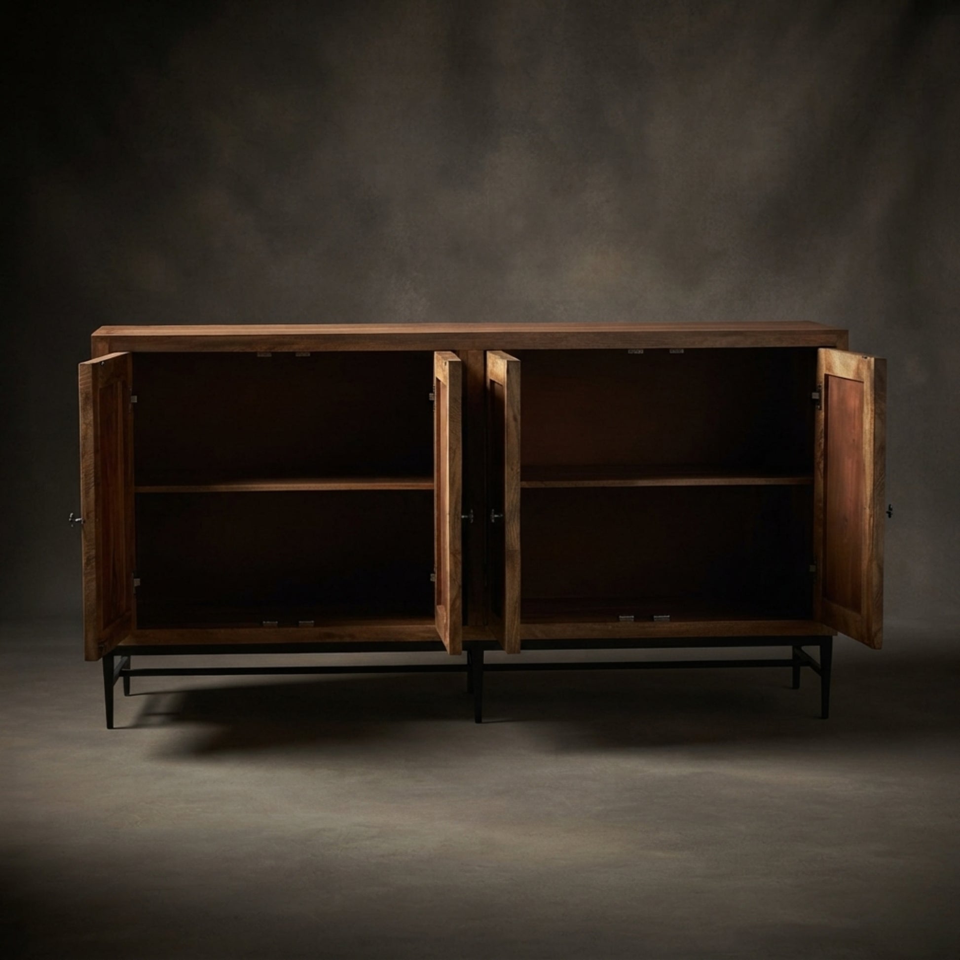 A rustic wooden sideboard cabinet with two open doors, showing dark wood shelves and black metal legs, set against a dark textured studio backdrop.