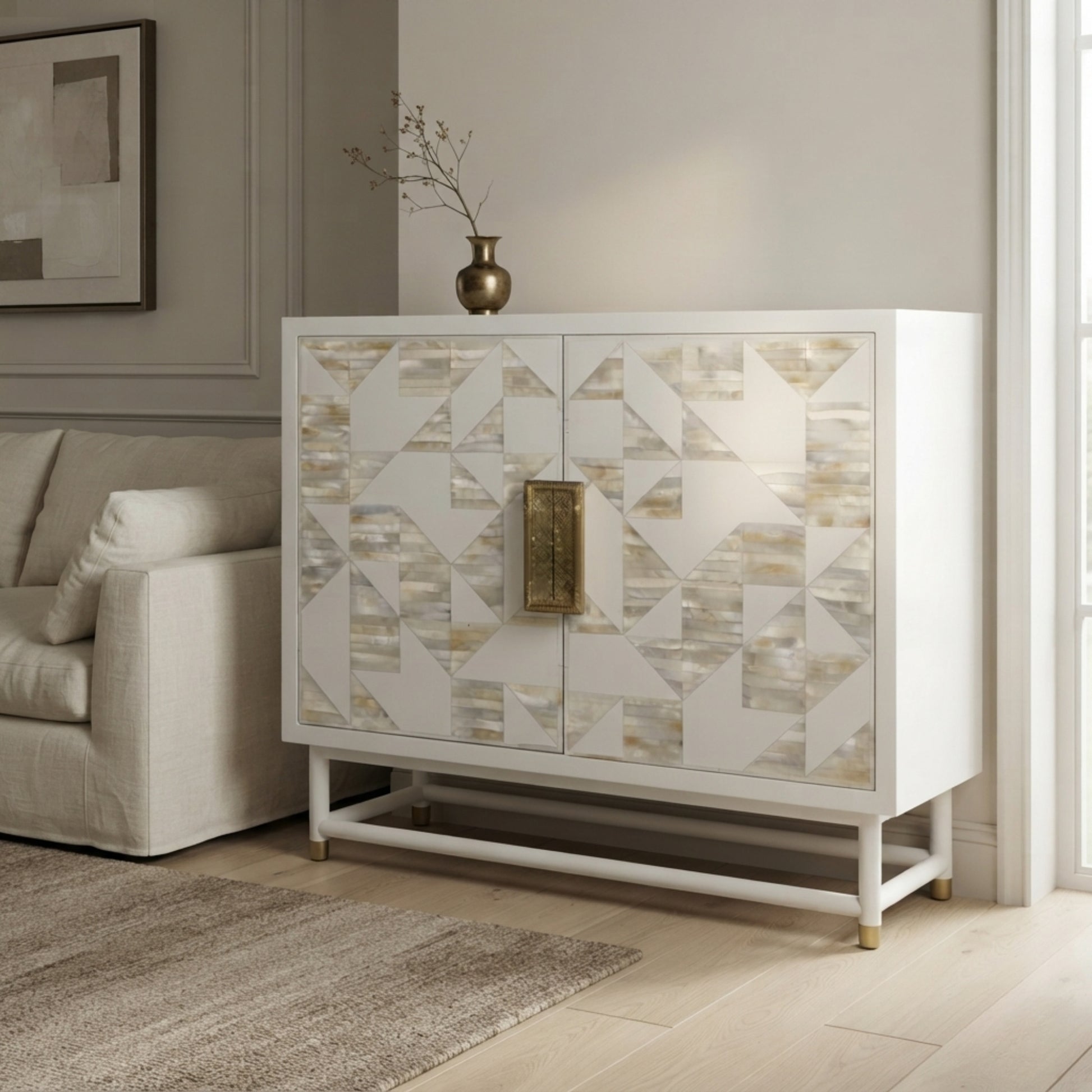 A white two-door cabinet with geometric shell-patterned doors and a central brass handle, styled in a modern living room next to a beige sofa.