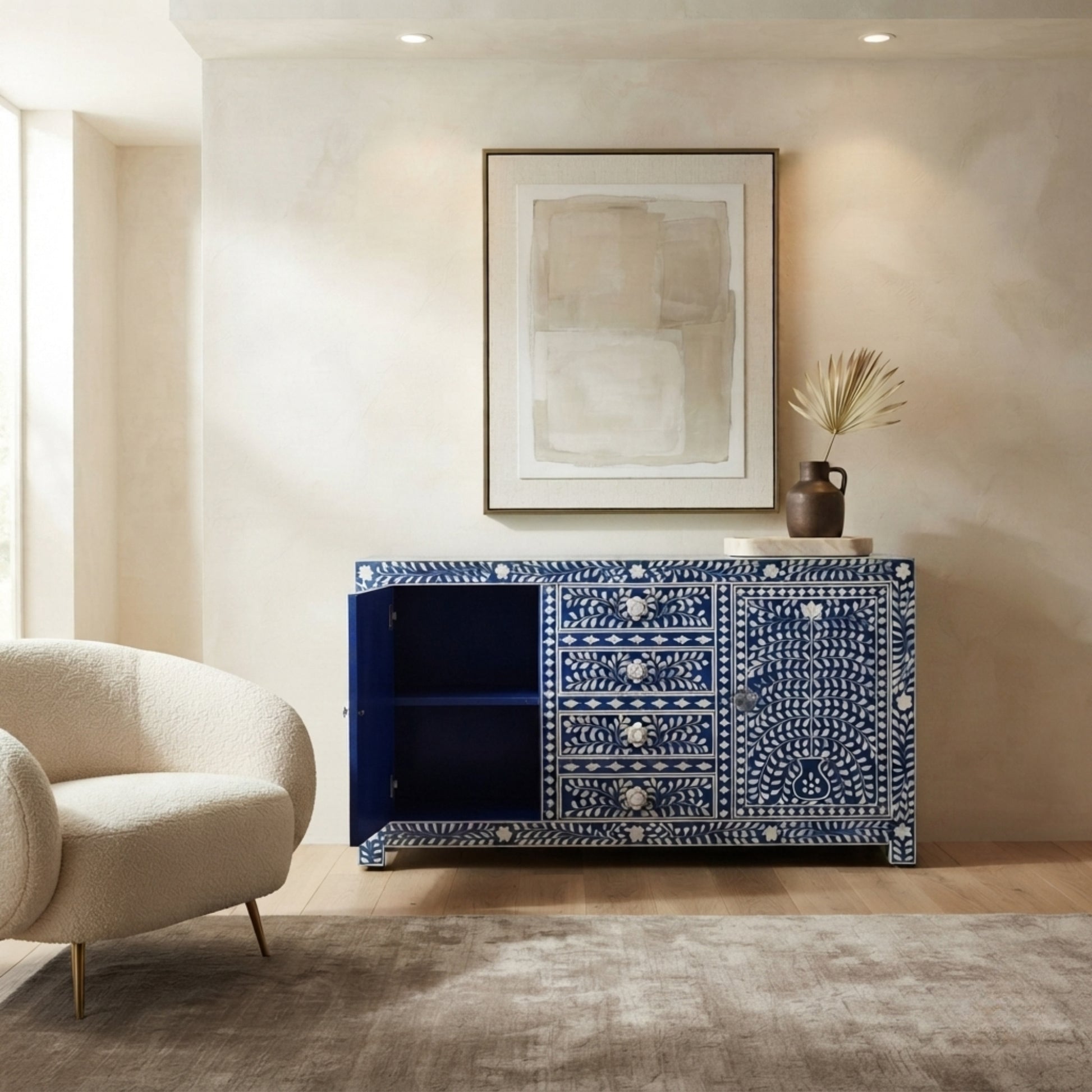 A blue and white bone-inlay sideboard cabinet in a styled room setting with a beige armchair, wall art, and a vase on top.