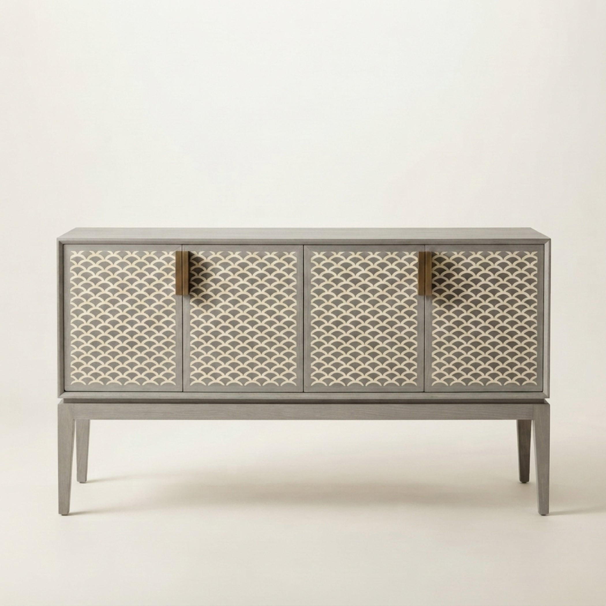 A modern sideboard cabinet with a gray frame and legs, featuring four doors decorated with a cream and gray geometric fish-scale pattern, accented by four vertical brass handles, set against a plain off-white background.