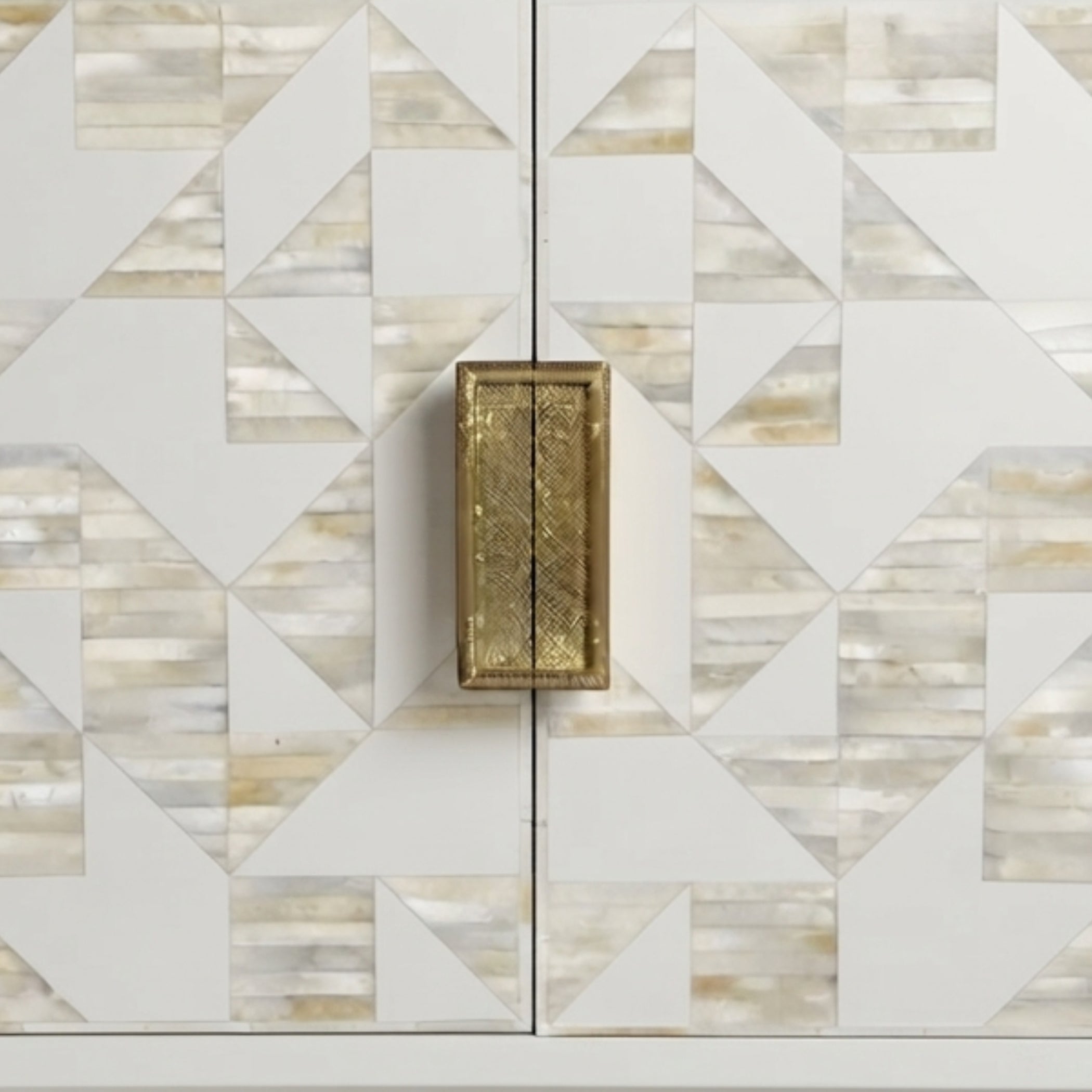 A close-up of a cabinet door featuring a geometric inlay pattern of white, beige, and light brown mother-of-pearl tiles, with a single rectangular brass handle centered on the split.