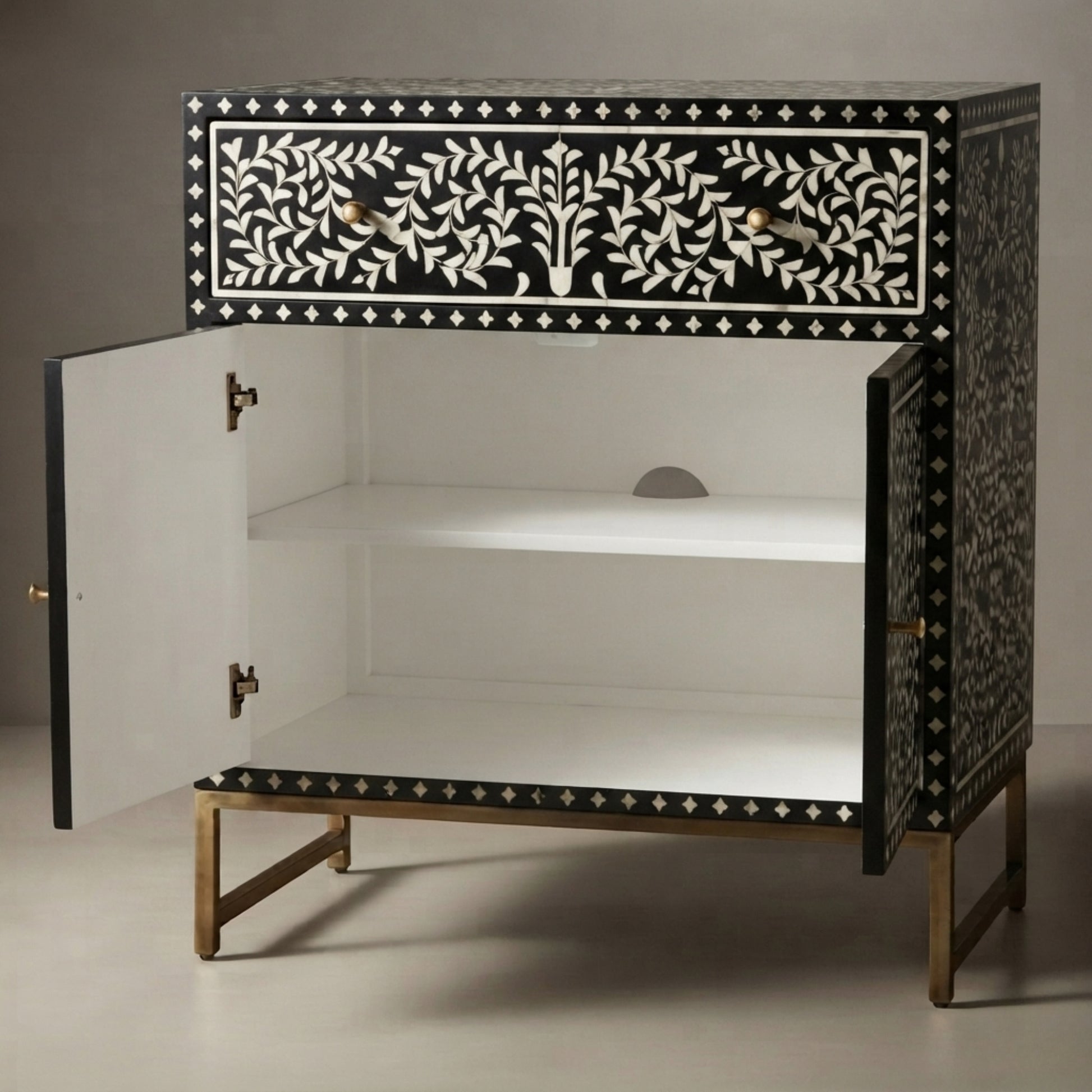 A black and white bone-inlay cabinet with gold metal legs, shown with its doors open to reveal a white interior and two shelves.