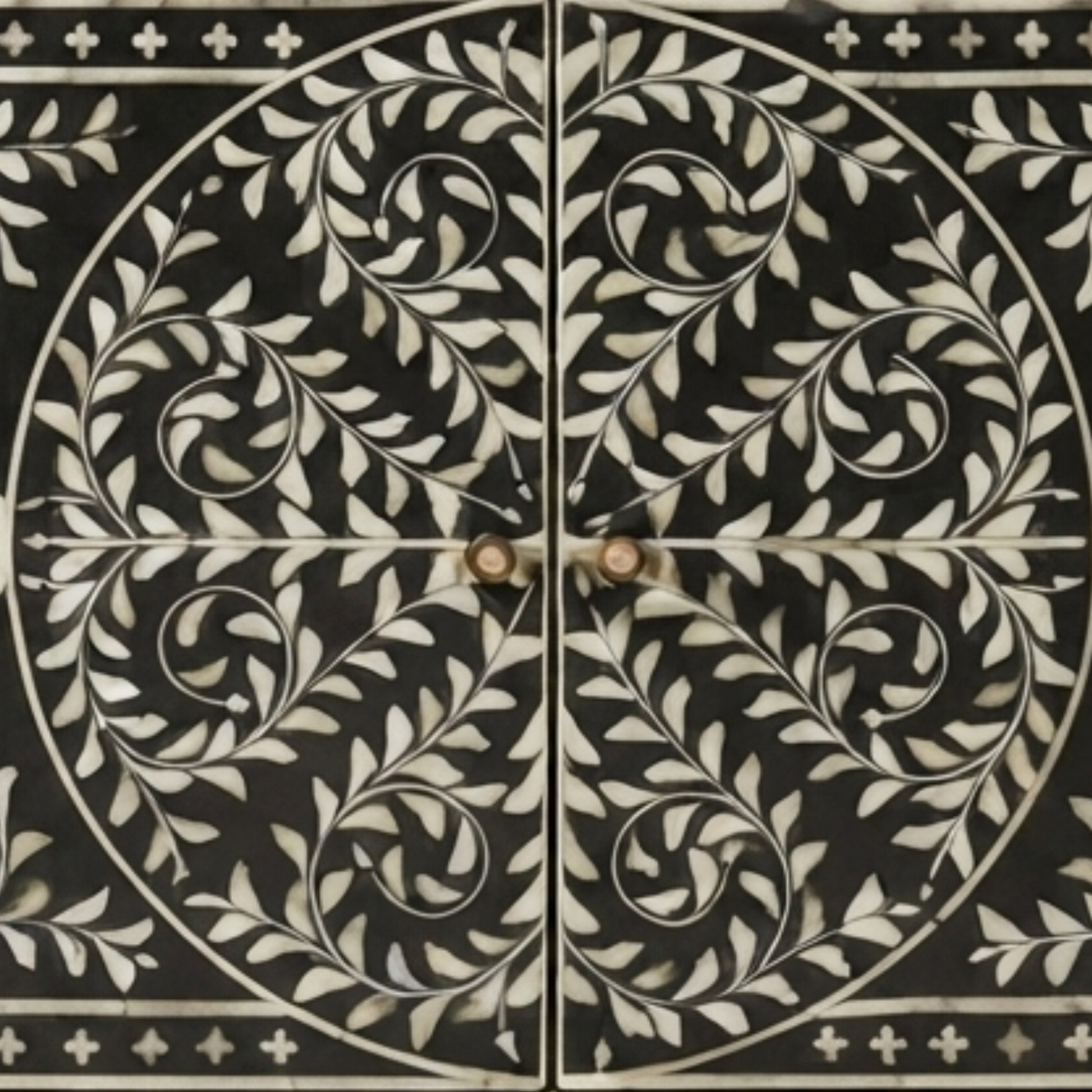 Black cabinet doors featuring an intricate white inlay pattern of scrolling leaves and vines, divided by a central cross with two round knobs.