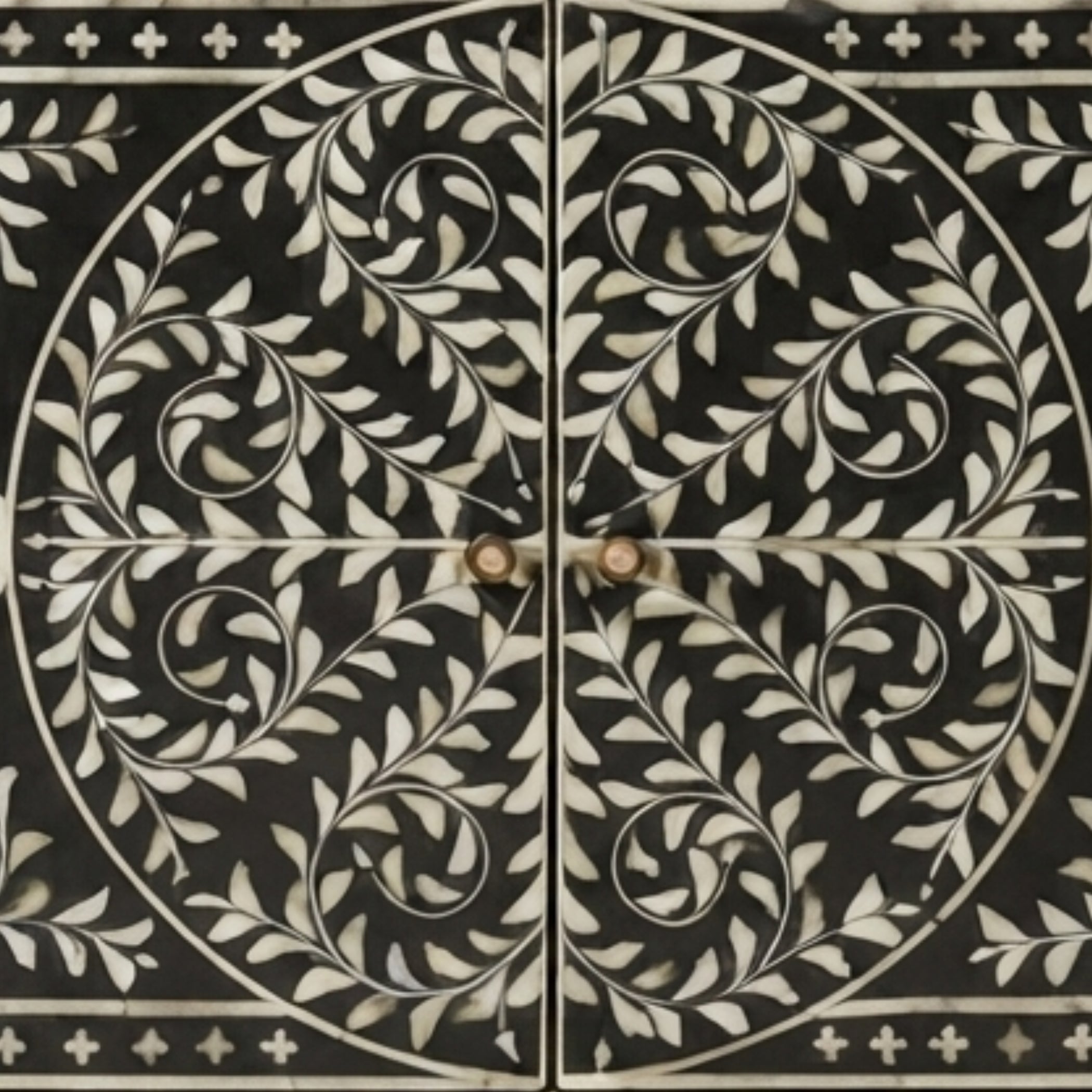 Black cabinet doors featuring an intricate white inlay pattern of scrolling leaves and vines, divided by a central cross with two round knobs.