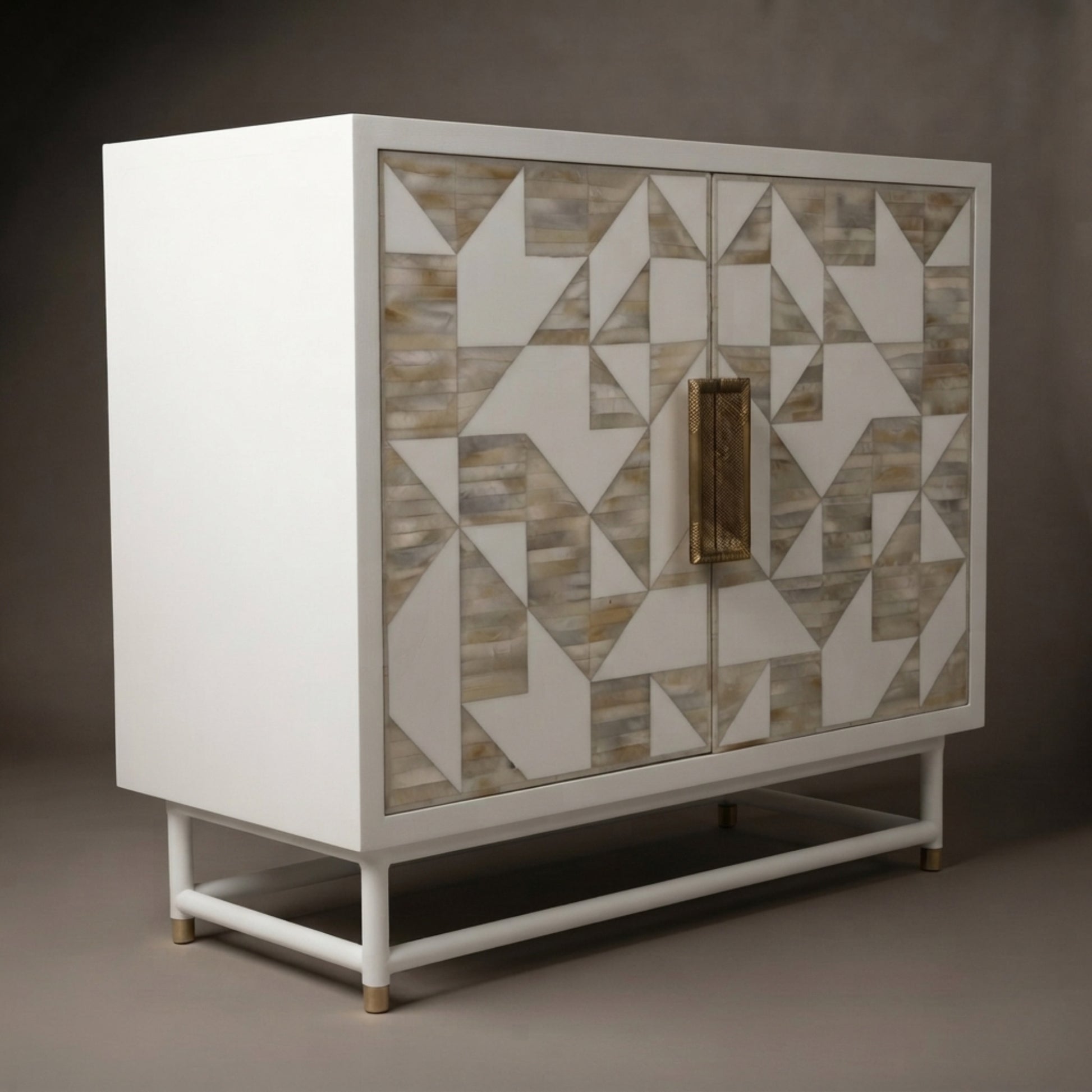 A modern white sideboard cabinet with a geometric bone-inlay pattern on the doors and a vertical brass handle, shown against a dark gray studio background.