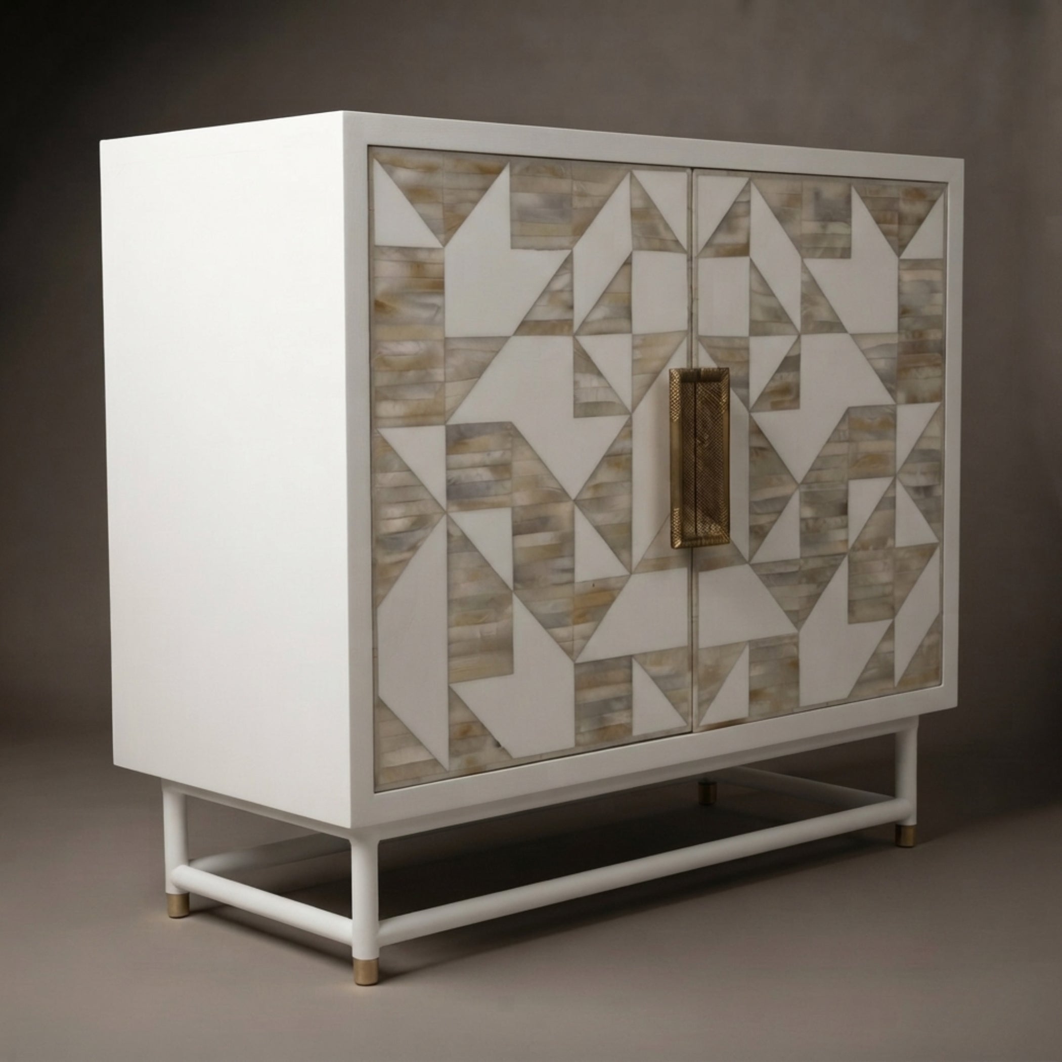 A modern white sideboard cabinet with a geometric bone-inlay pattern on the doors and a vertical brass handle, shown against a dark gray studio background.