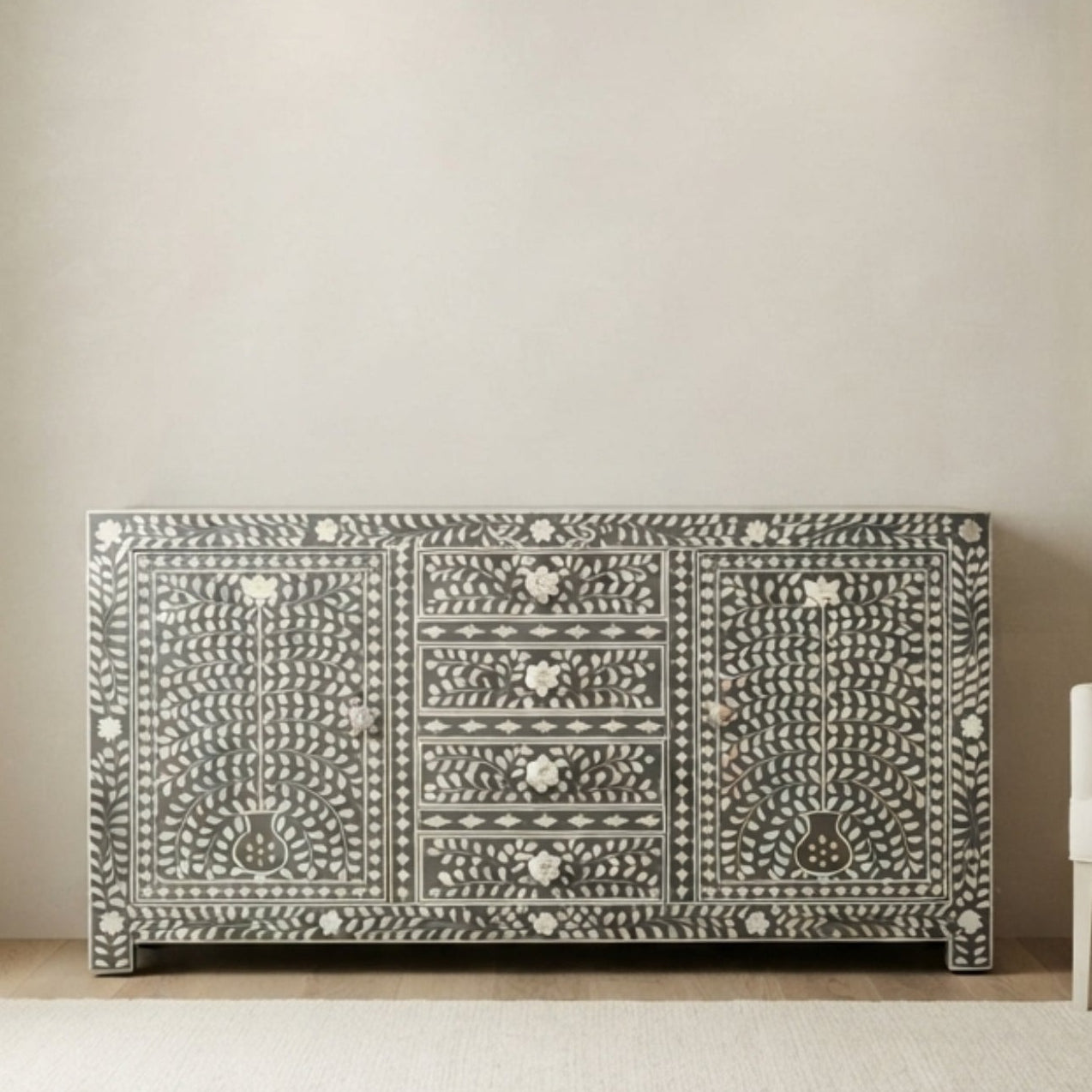 A decorative sideboard or credenza with an intricate black and white bone-inlay pattern, styled in a minimalist modern living room next to a white armchair and a light beige rug.