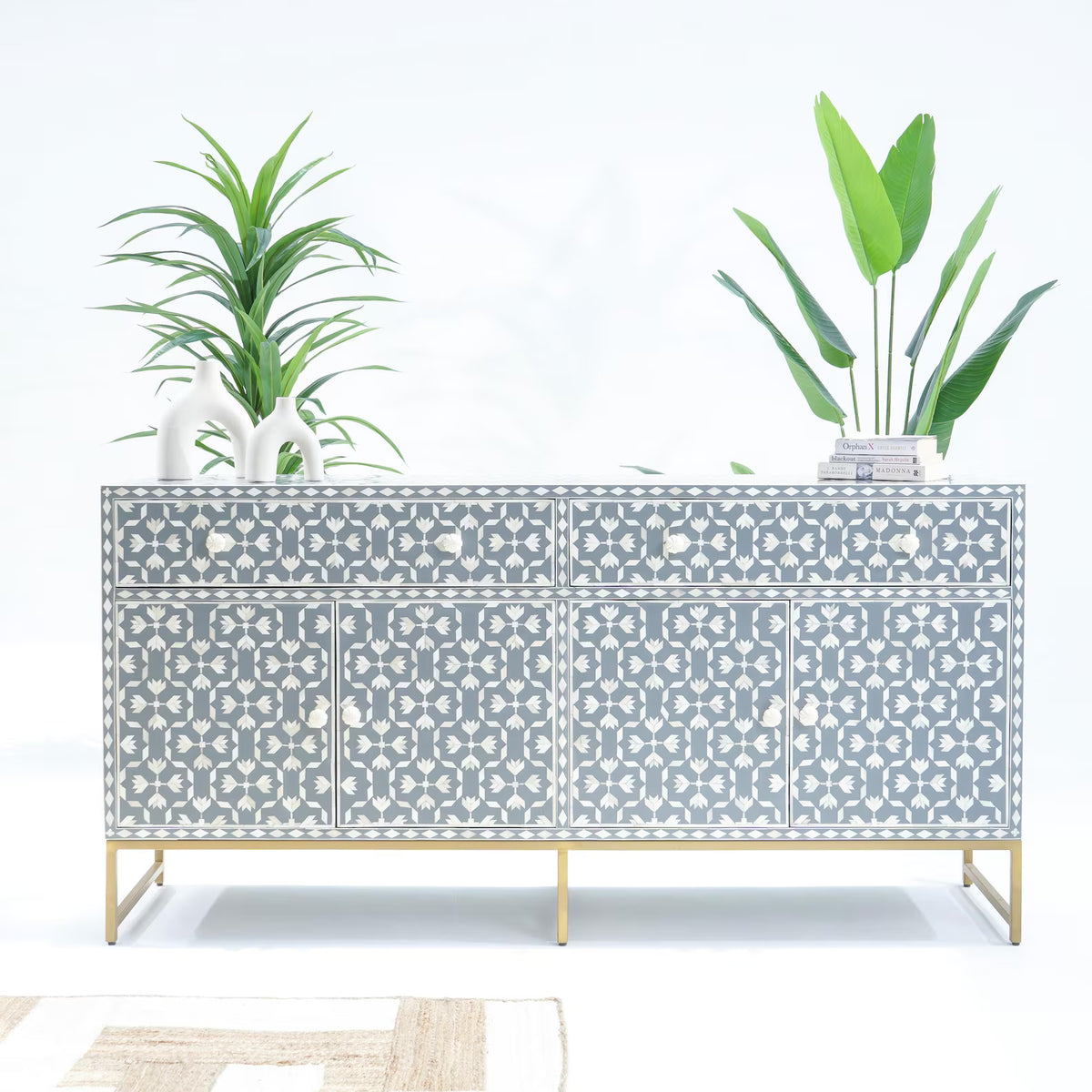 Decorative sideboard with a geometric pattern, gold legs, and potted plants on a white background