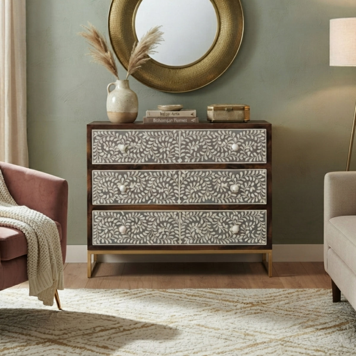 A three-drawer chest of drawers with a dark wood frame and white bone-patterned drawer fronts, styled in a living room setting with a round mirror, vase, and pampas grass.