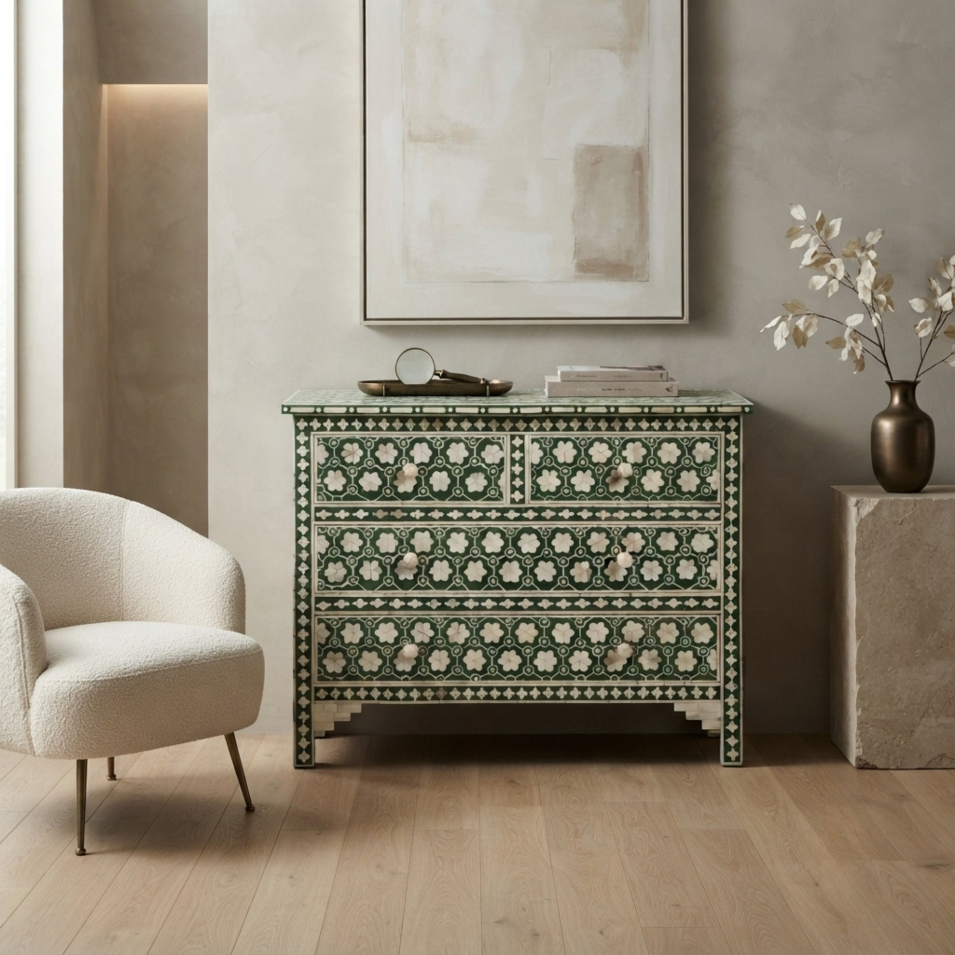 An ornate green and cream mother-of-pearl chest of drawers styled in a modern, neutral-toned living room next to a cream armchair.