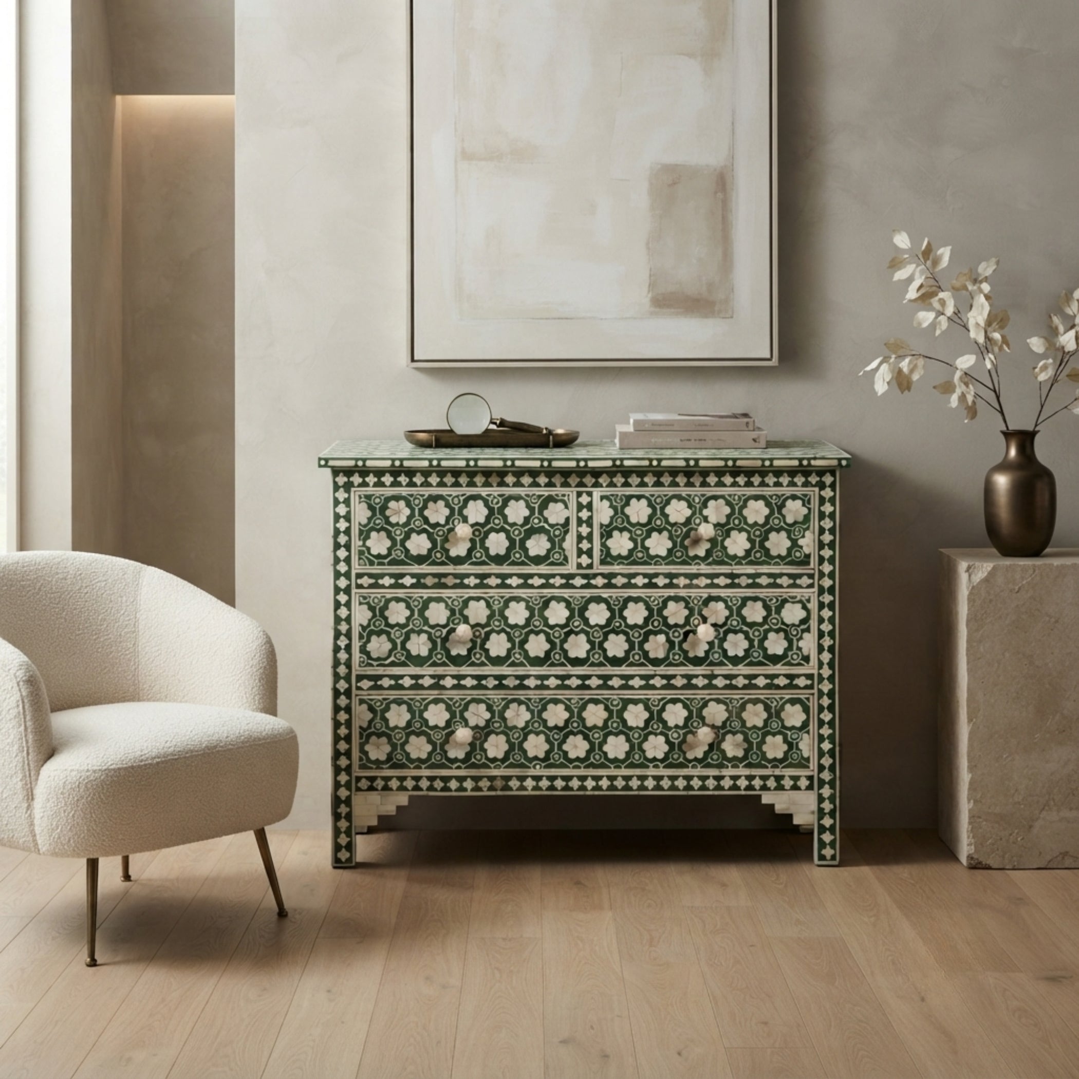 An ornate green and cream mother-of-pearl chest of drawers styled in a modern, neutral-toned living room next to a cream armchair.
