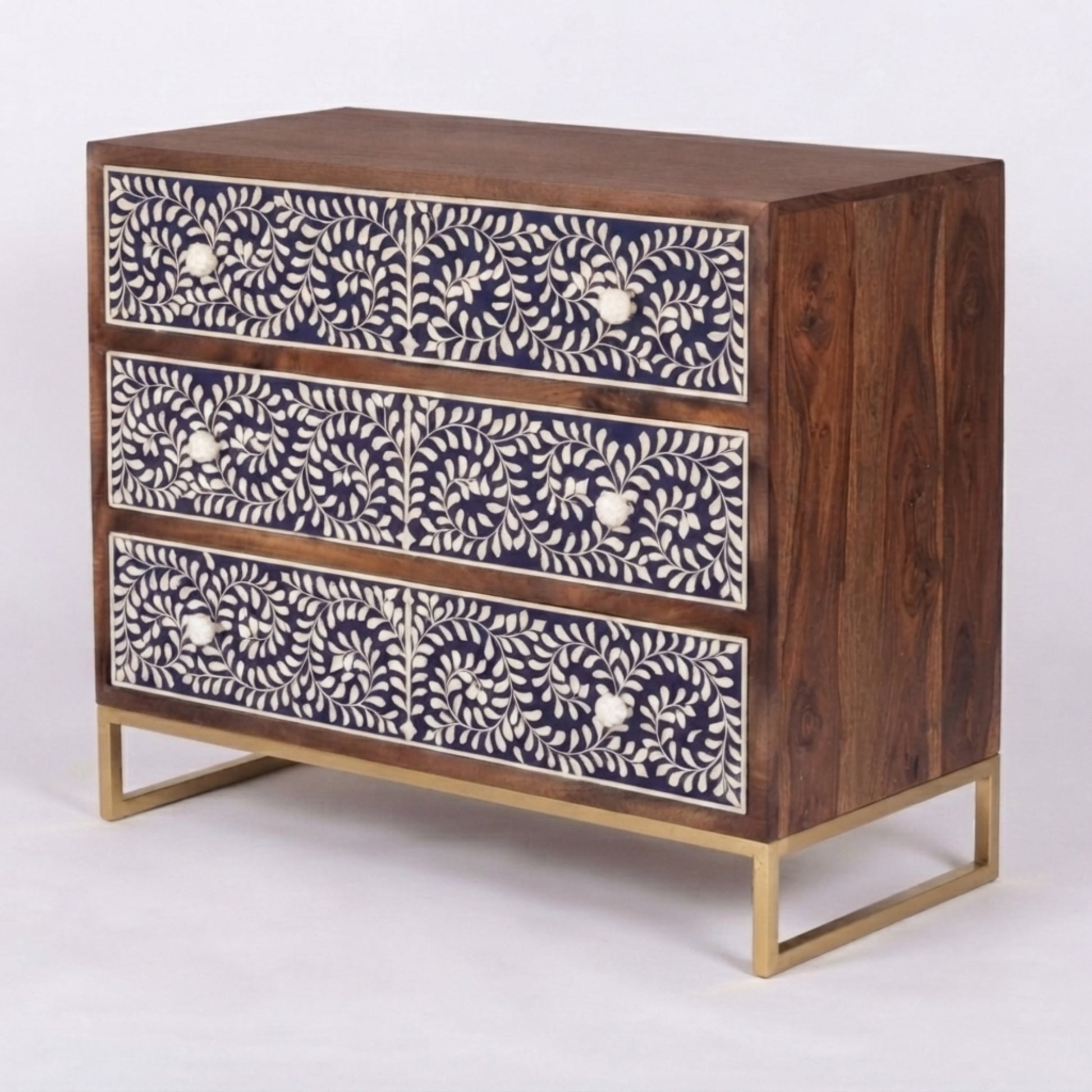 A three-drawer wooden chest of drawers with dark brown wood, navy blue and white floral bone inlay on the drawer fronts, and a gold metal frame and legs, shown on a light gray background.