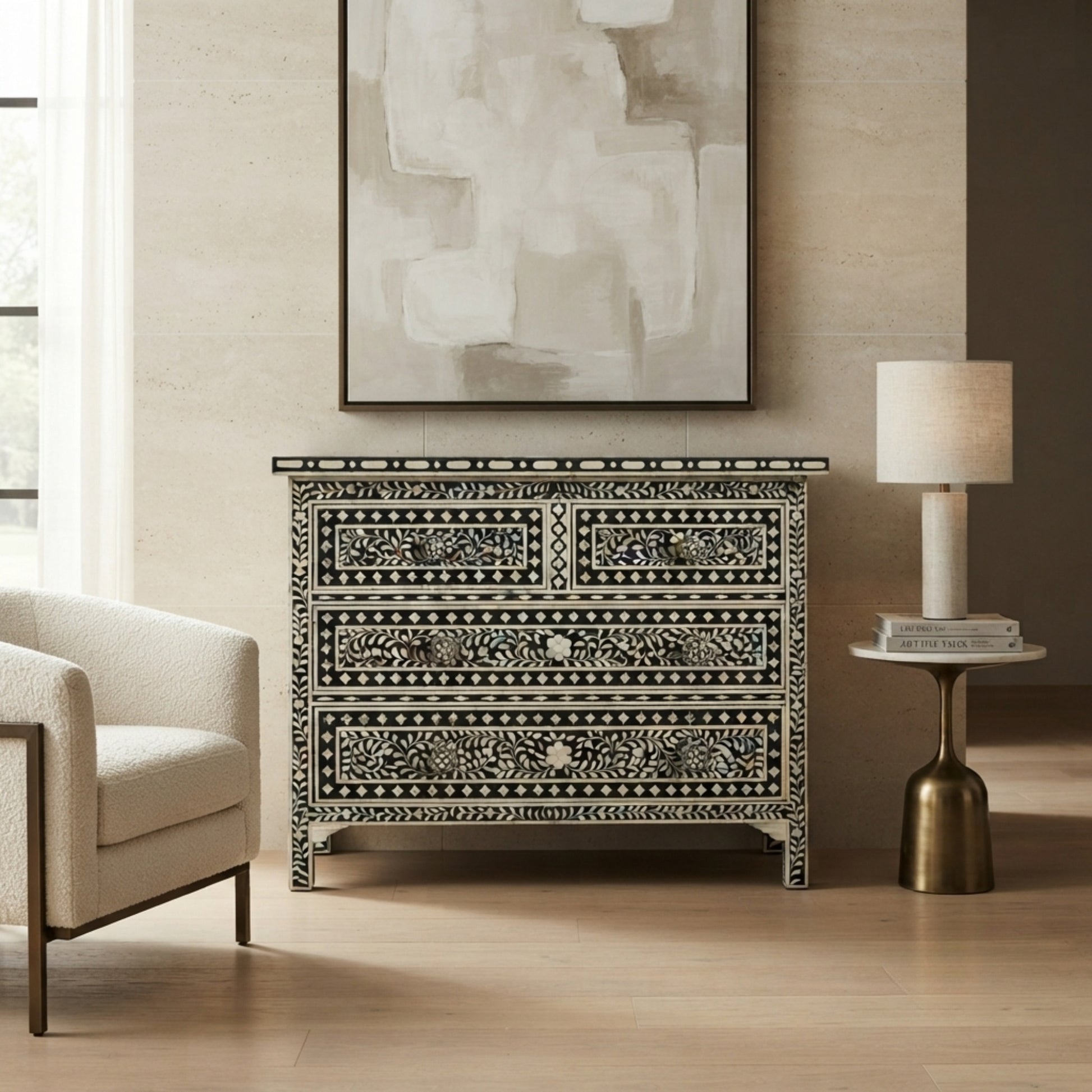 An ornate black and white bone-inwood chest of drawers styled in a modern living room setting with a beige armchair, a side table with a lamp, and a large abstract painting on the wall.